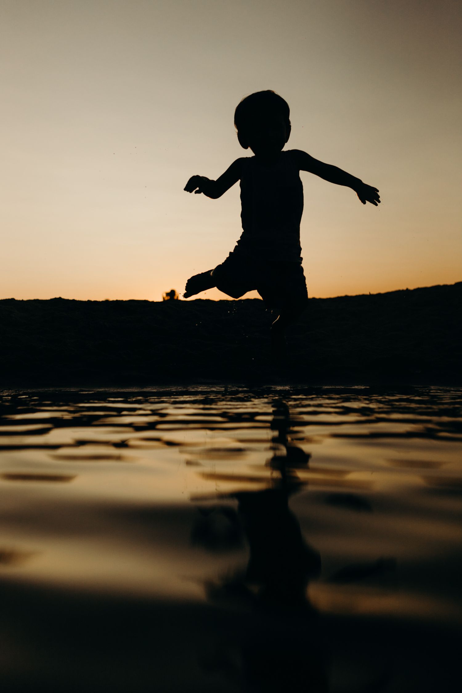 Silhouette of a child playing at the beach during sunset with their reflection in the shallow water.