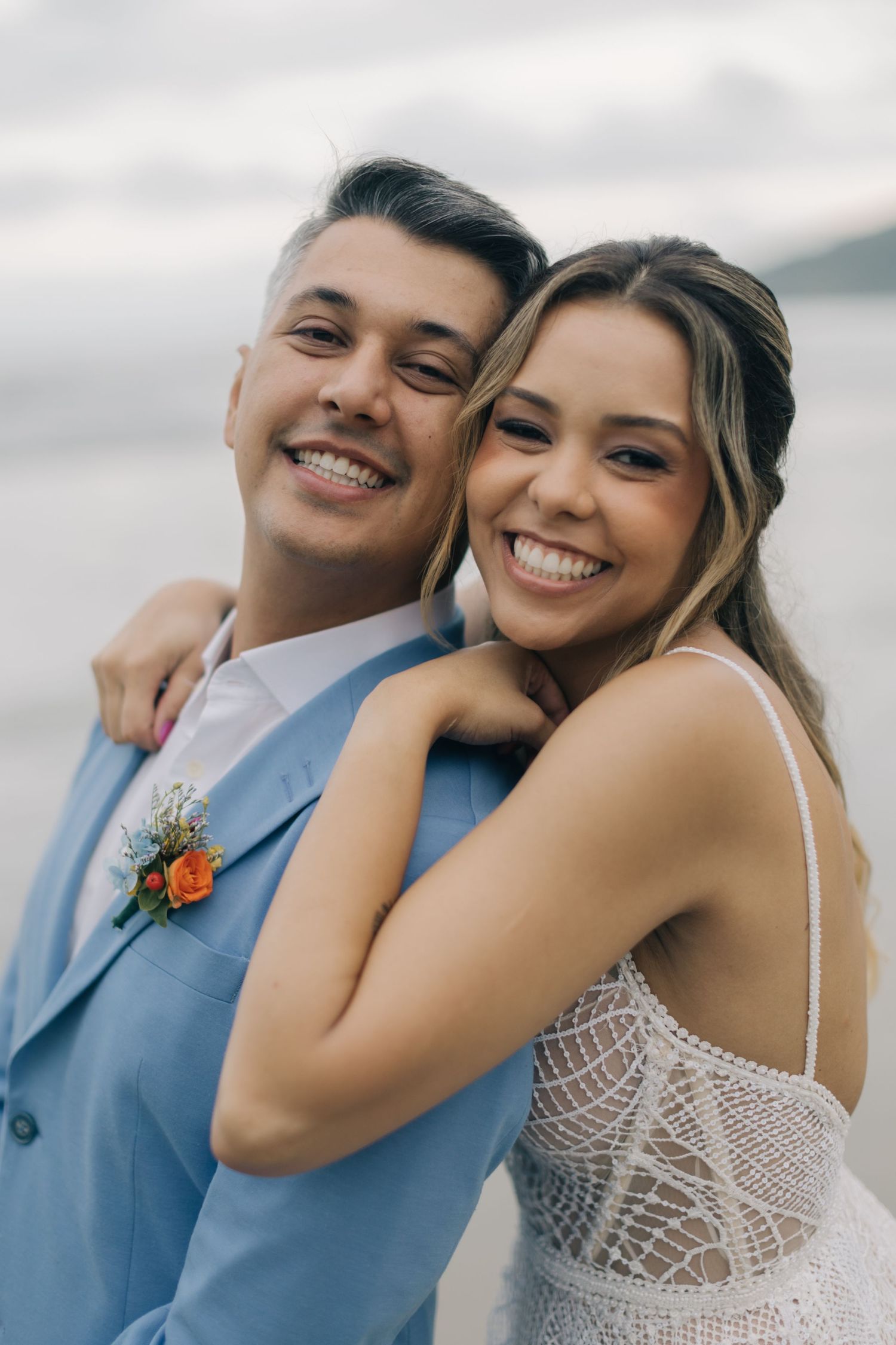 A joyful couple in wedding attire share an intimate moment by the ocean.