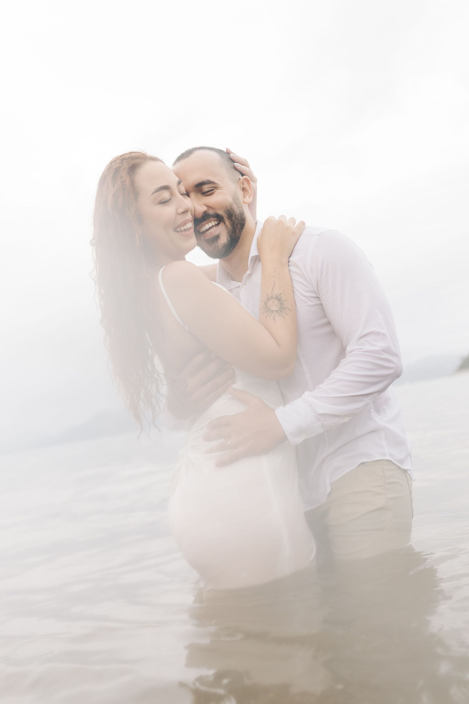 A loving couple shares laughter while embracing in shallow ocean waters.