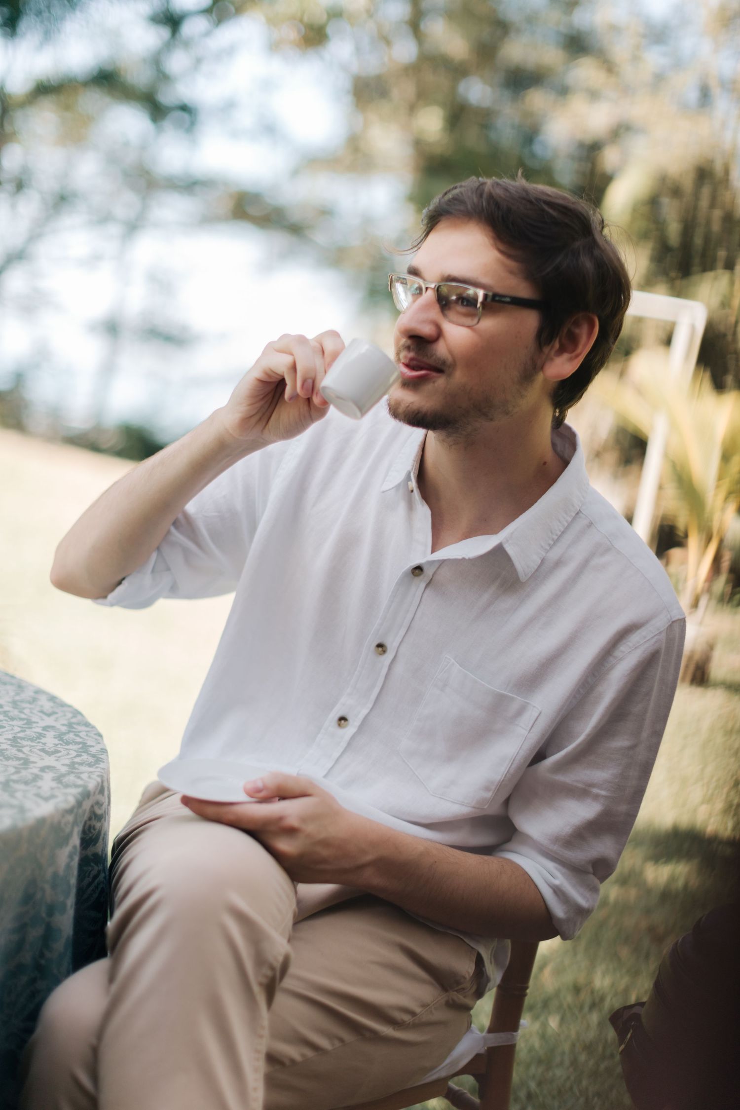 Man in white shirt sitting outdoors talking on phone during casual moment.
