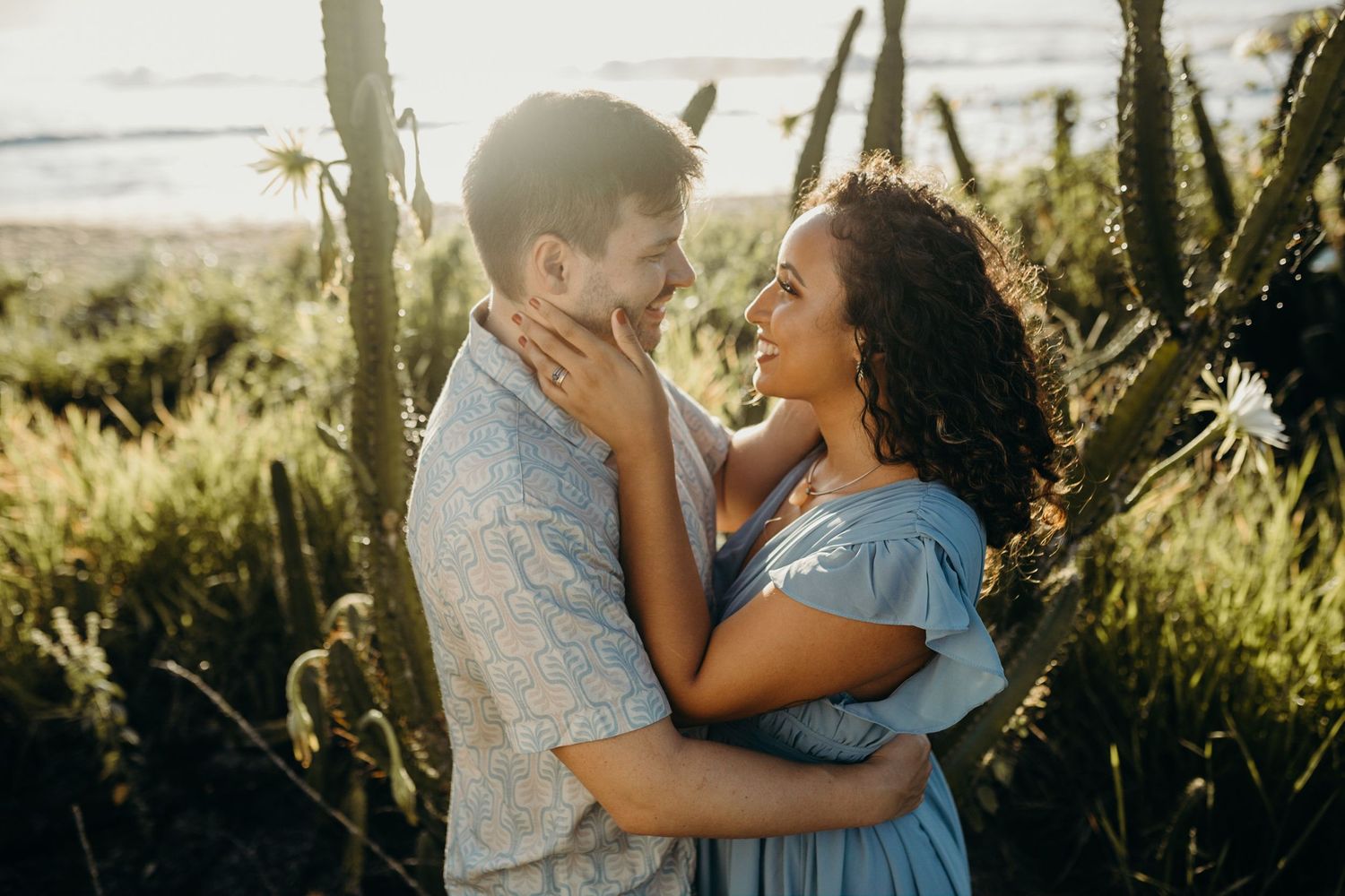 Couple in blue outfits sharing intimate moment among coastal vegetation.