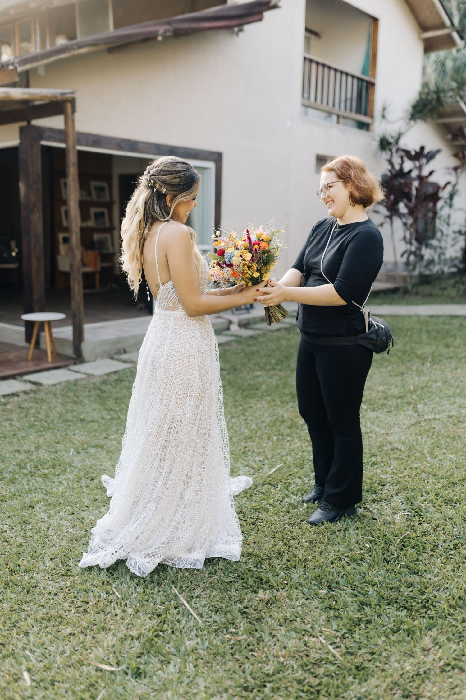 A wedding moment captured on a lawn as a bouquet is exchanged between two people.