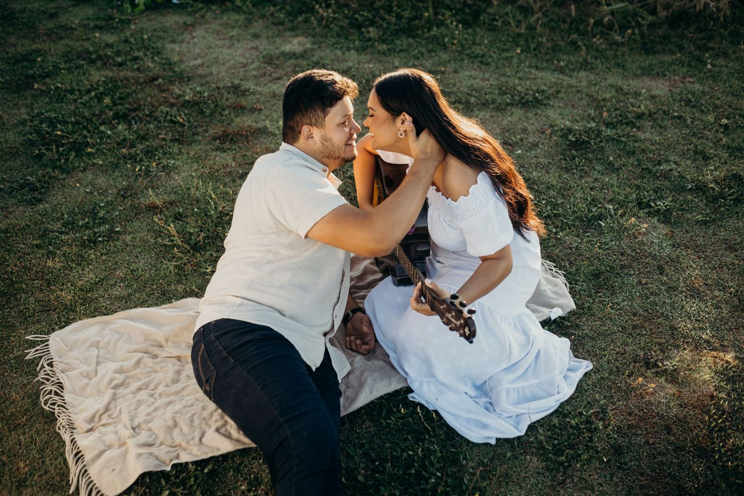Couple sharing tender moment while sitting on blanket outdoors with guitar.