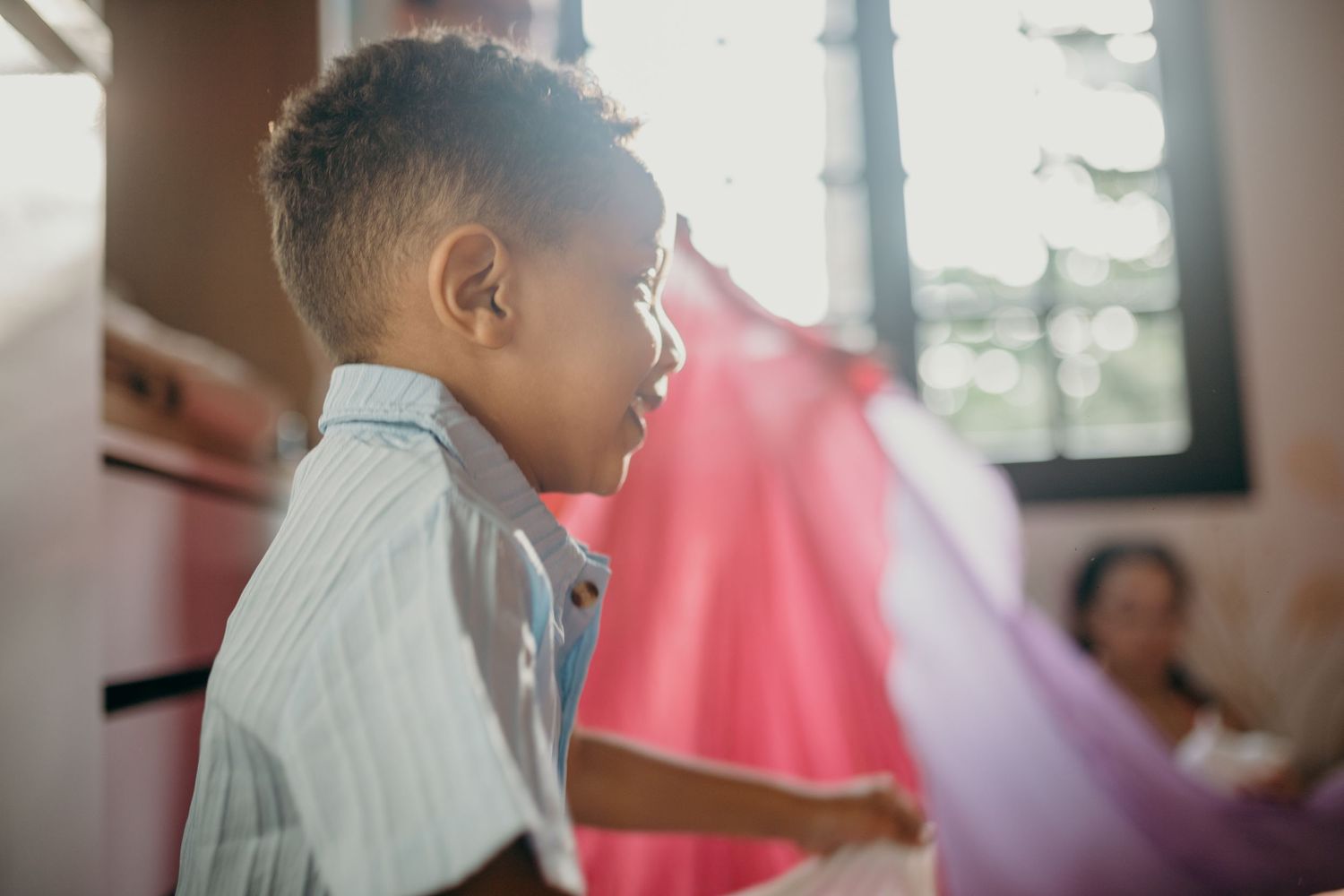 Child in white shirt gazes intently to the side with colorful fabrics in background.
