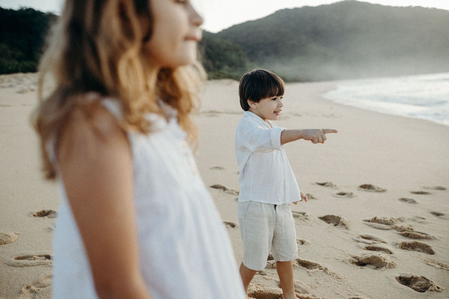 People in white clothing on a misty beach with mountains in the distance.