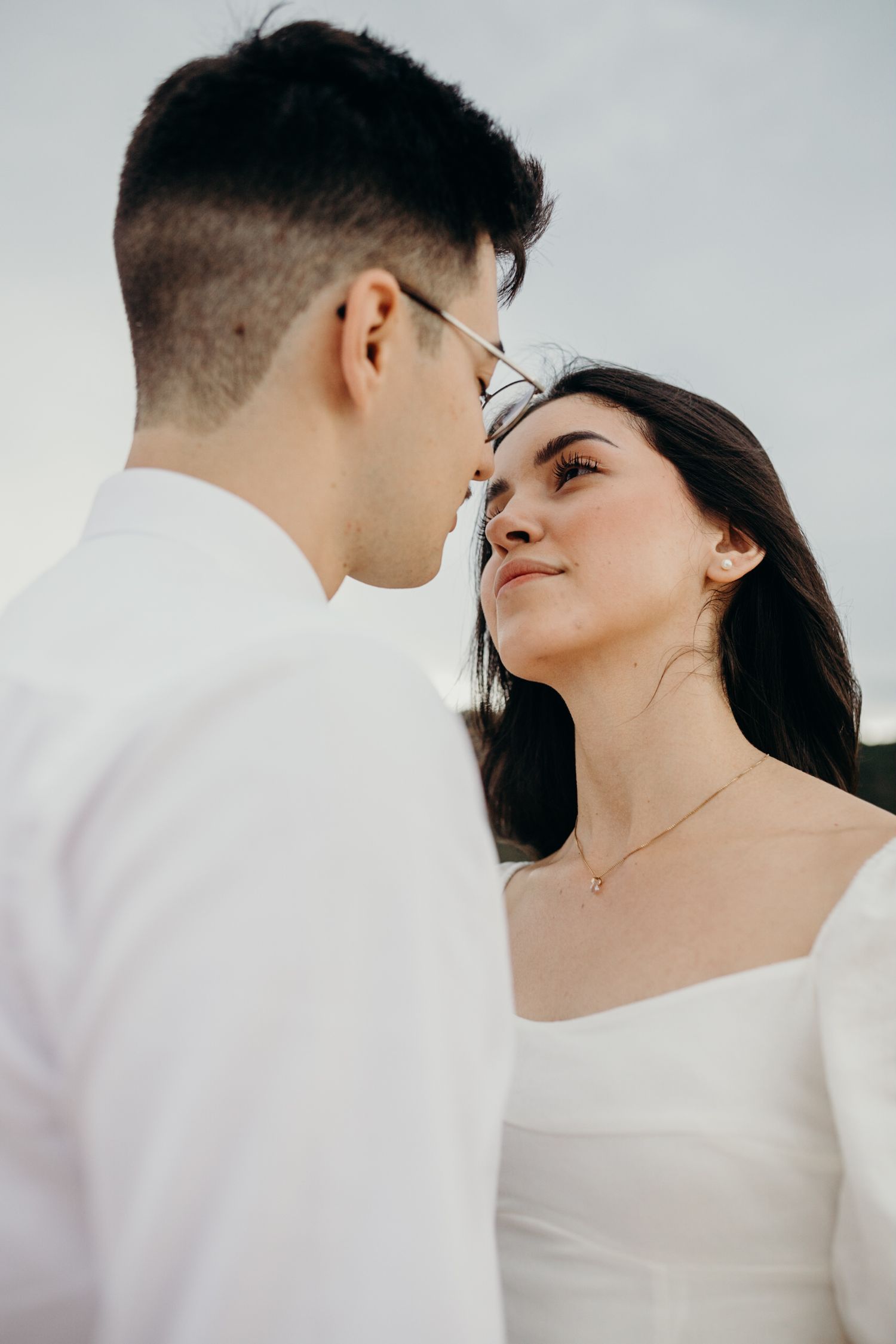 An intimate close-up portrait of a couple in white attire sharing a tender moment.