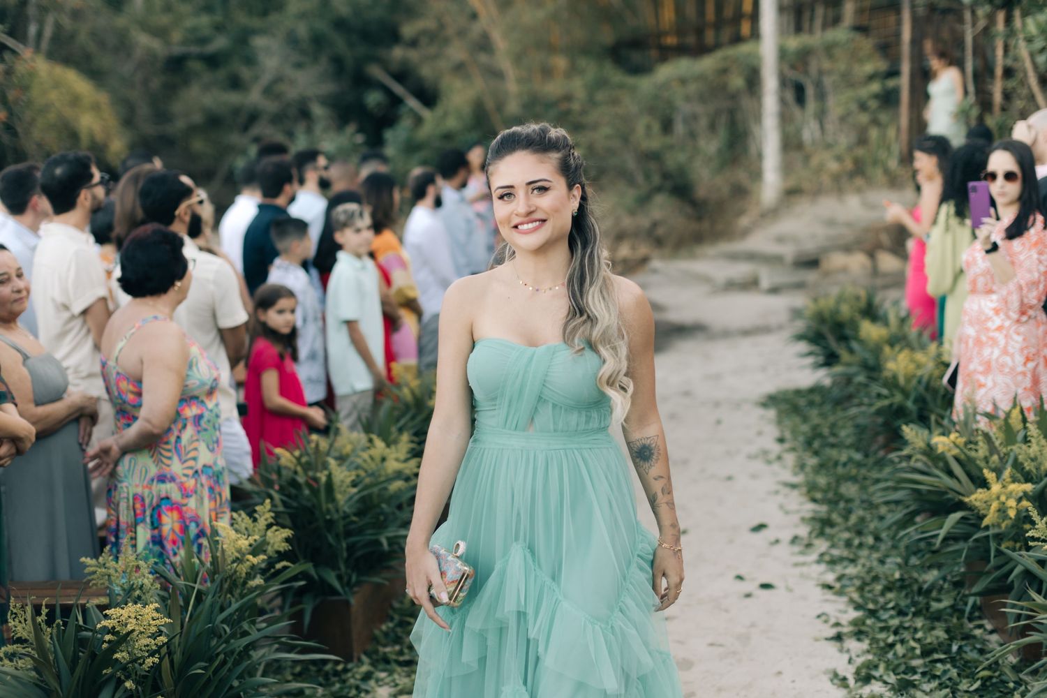 Wedding guests stroll down a garden pathway lined with green foliage.