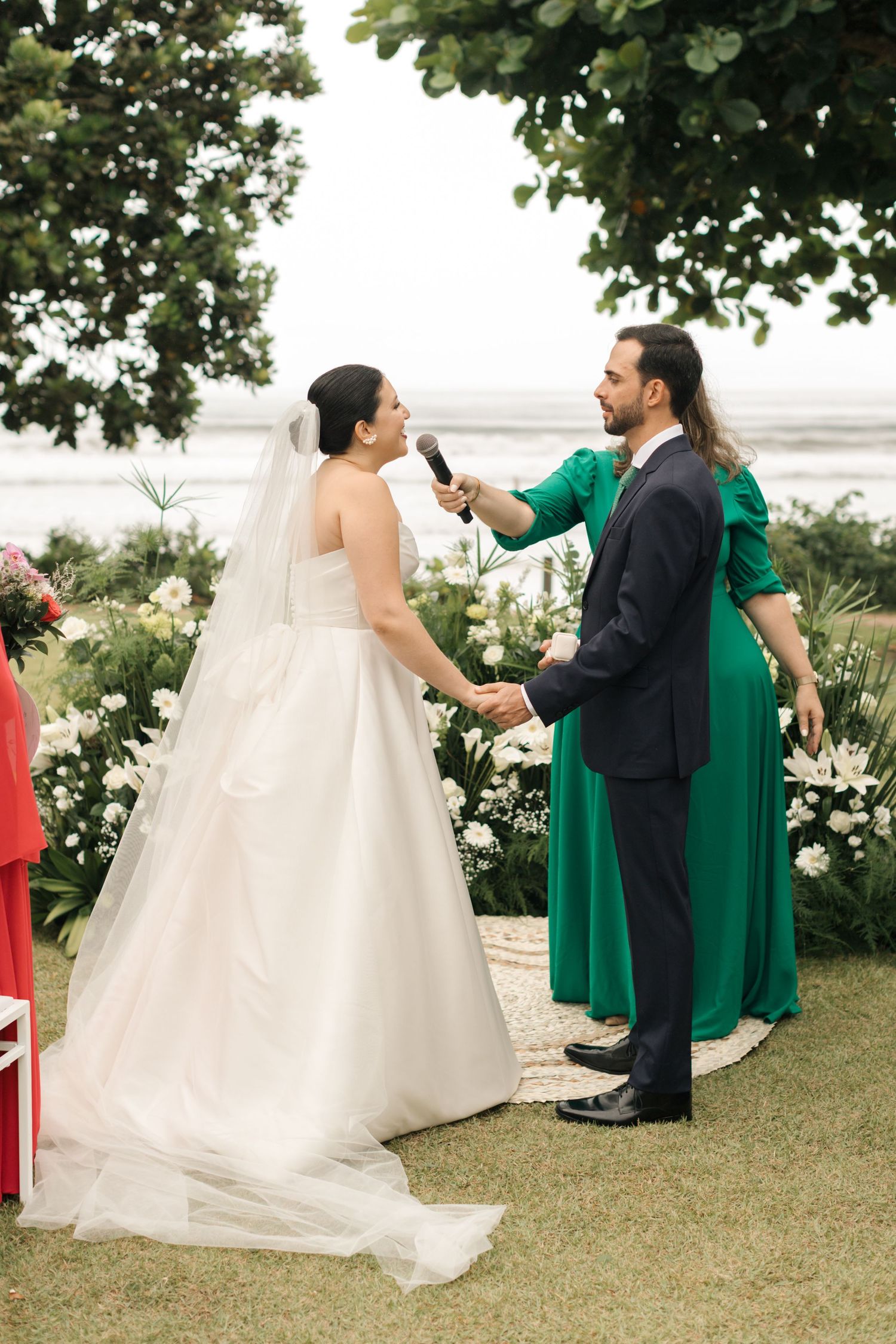 Wedding guests seated outdoors in emerald green attire during garden ceremony.
