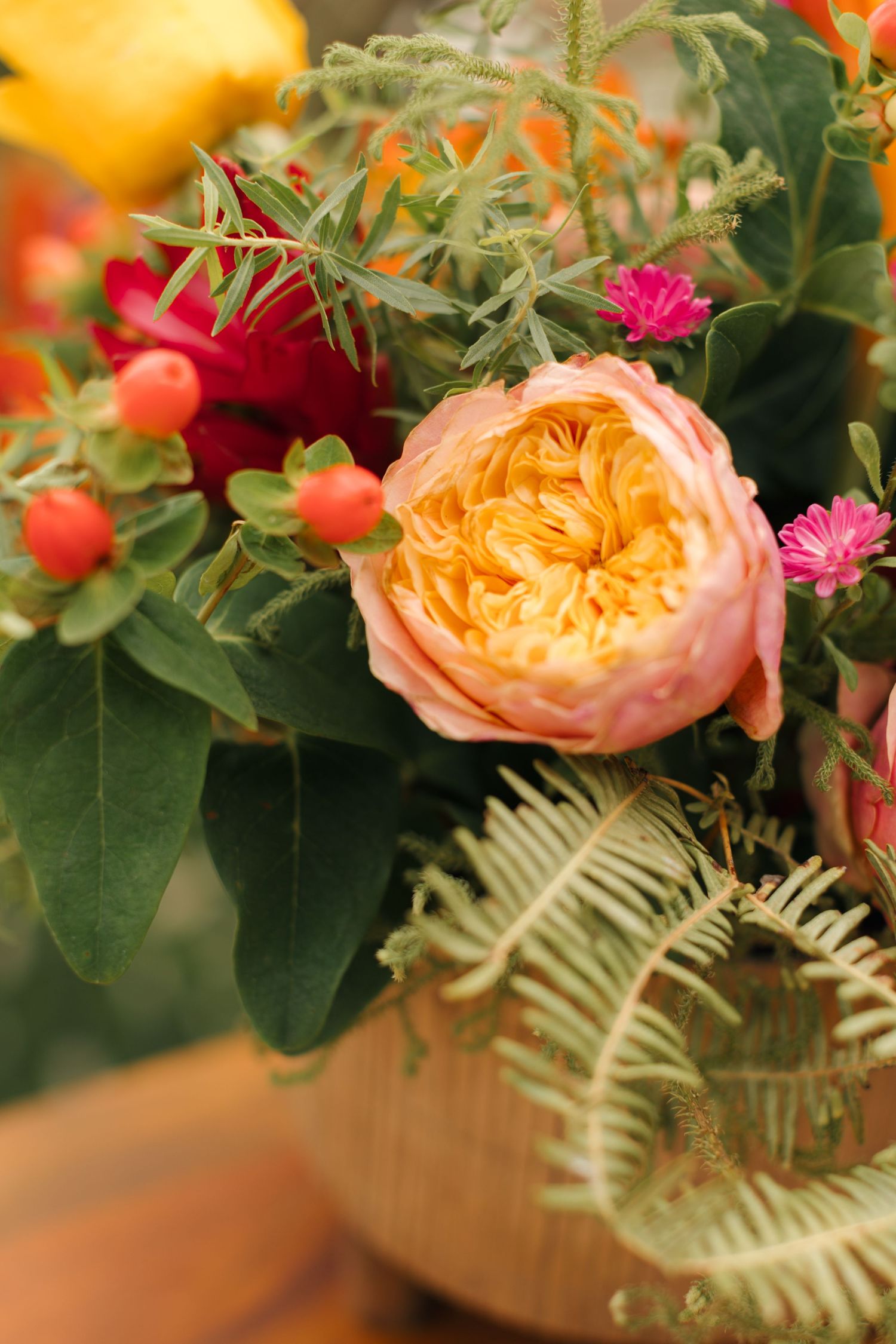 Peach-colored garden rose with small pink flowers and red berries in a rustic floral arrangement.