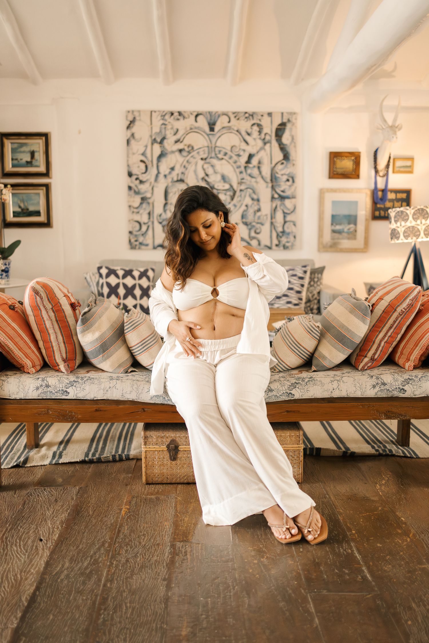 A person in a white dress reclines on a rustic wooden bench with striped cushions and decorative pillows.