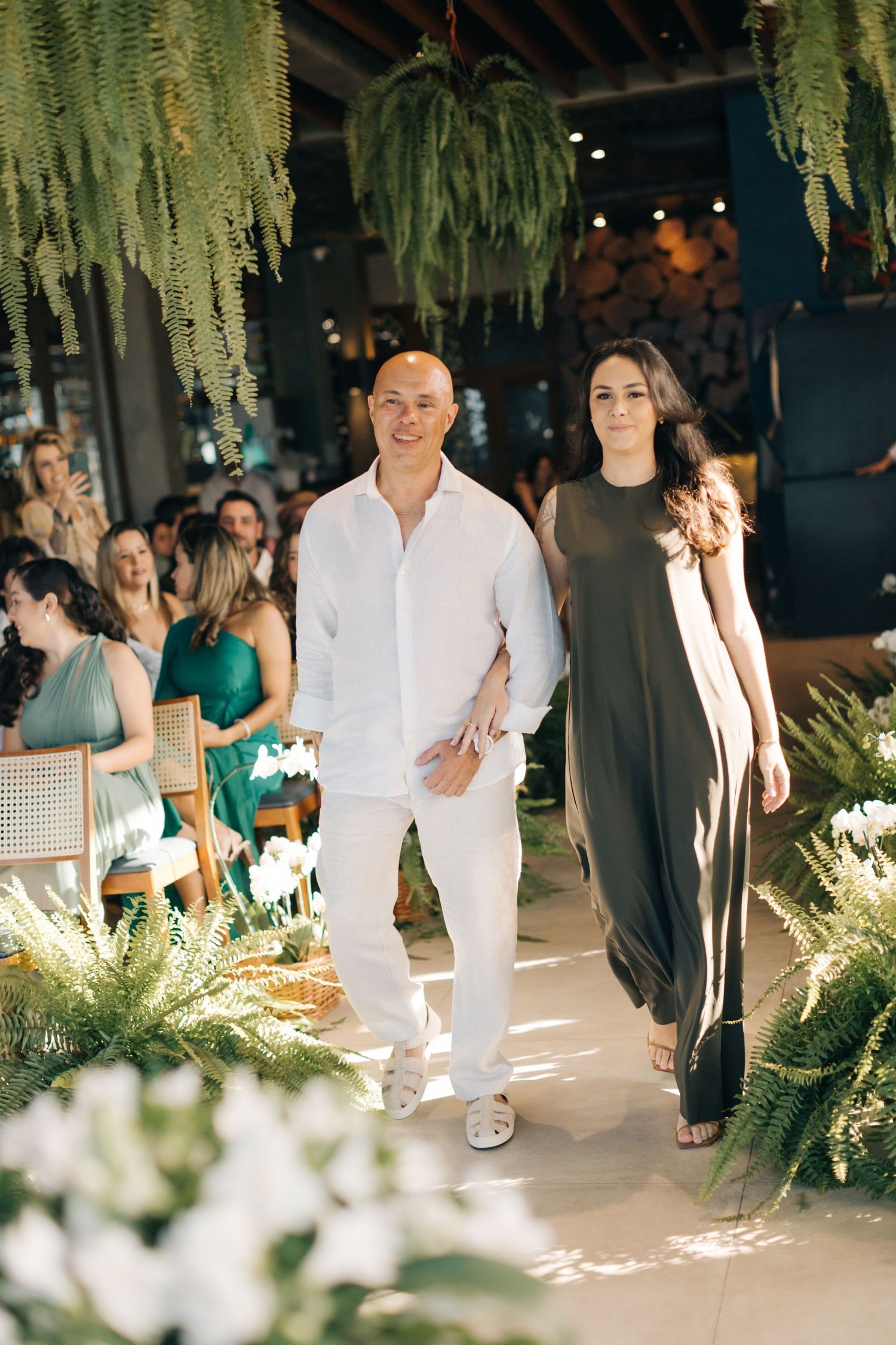Wedding guests walking down an aisle decorated with hanging greenery and white flowers.
