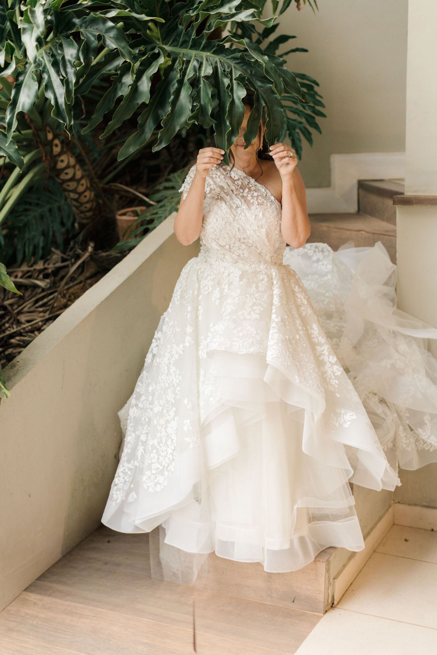 White wedding dress with lace details displayed against tropical foliage backdrop.