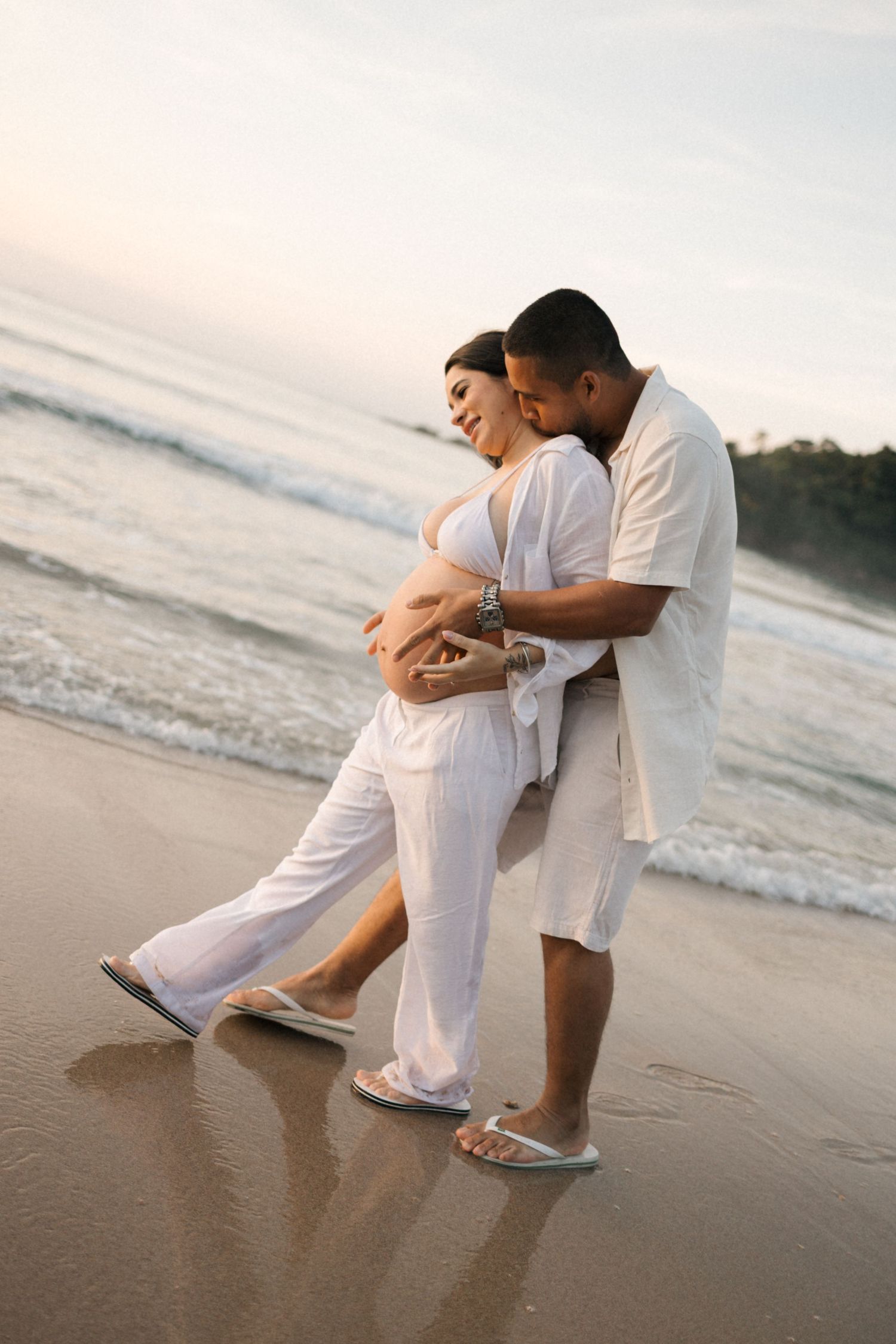 Joyful couple in white embracing and dancing together on sandy beach.