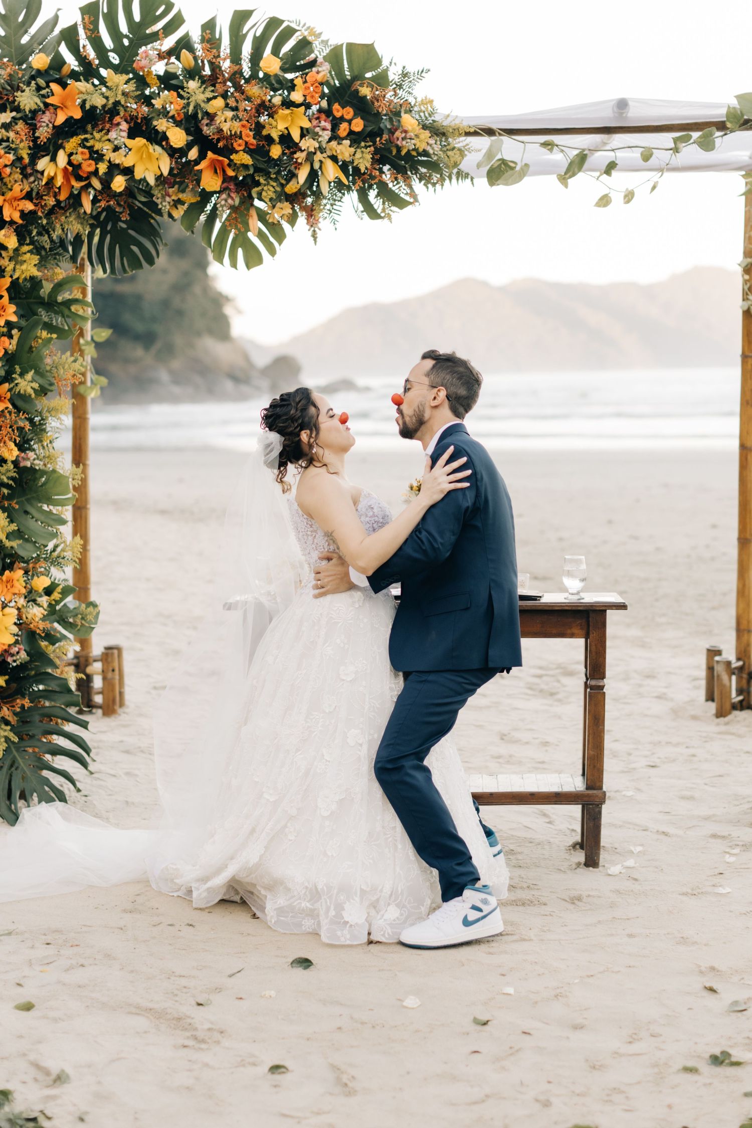 Couple shares a playful dance moment under a tropical flower arch during their beach wedding.