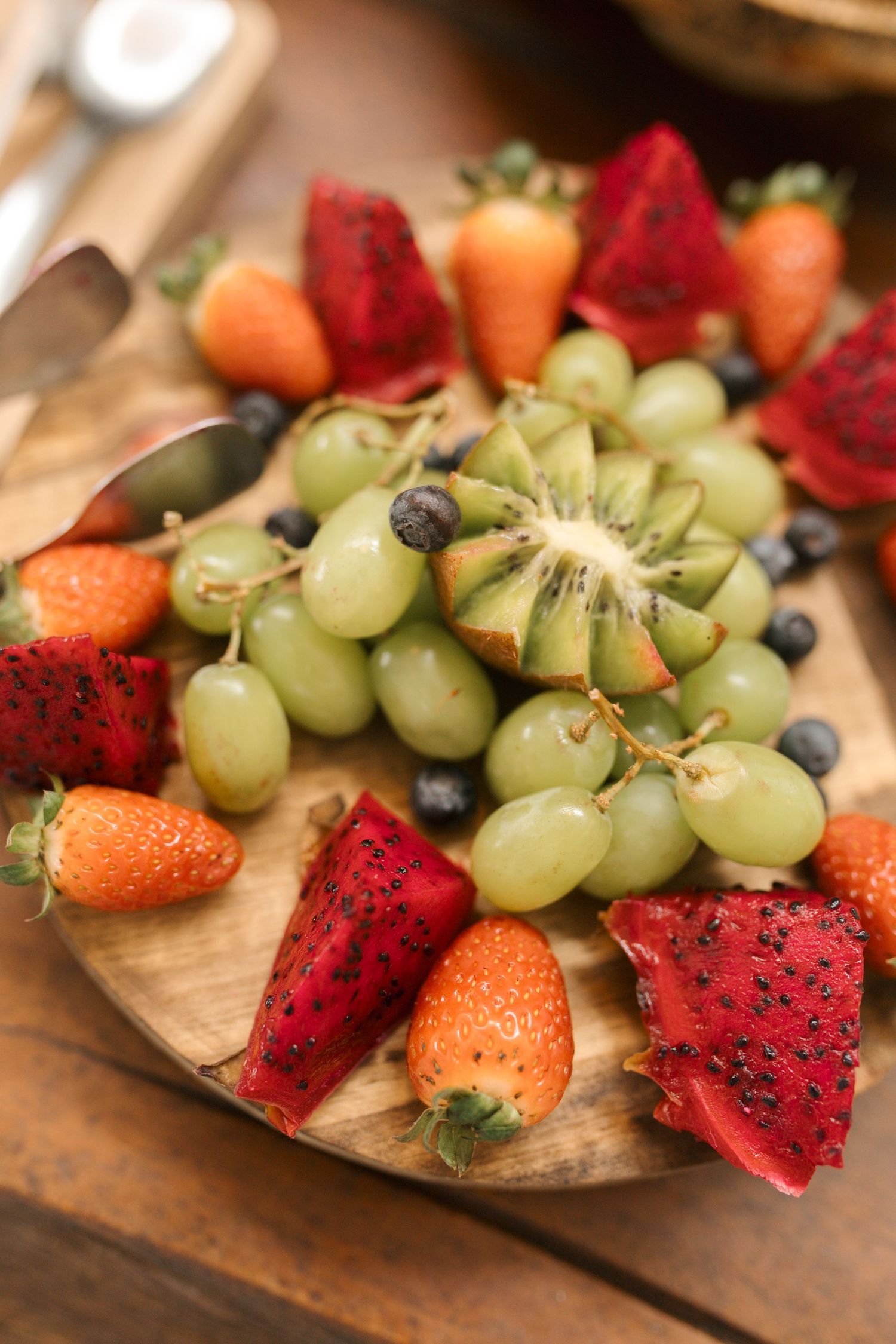 Fresh fruit platter with dragon fruit, strawberries, grapes and citrus arranged on wooden board.
