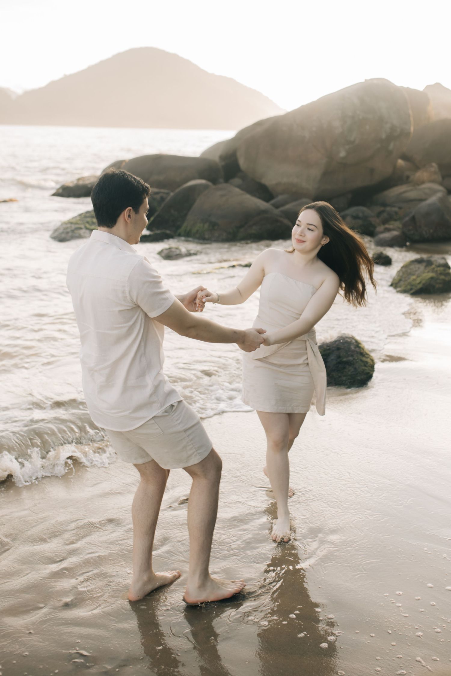 Couple dancing and playing in shallow water on rocky beach at sunset.