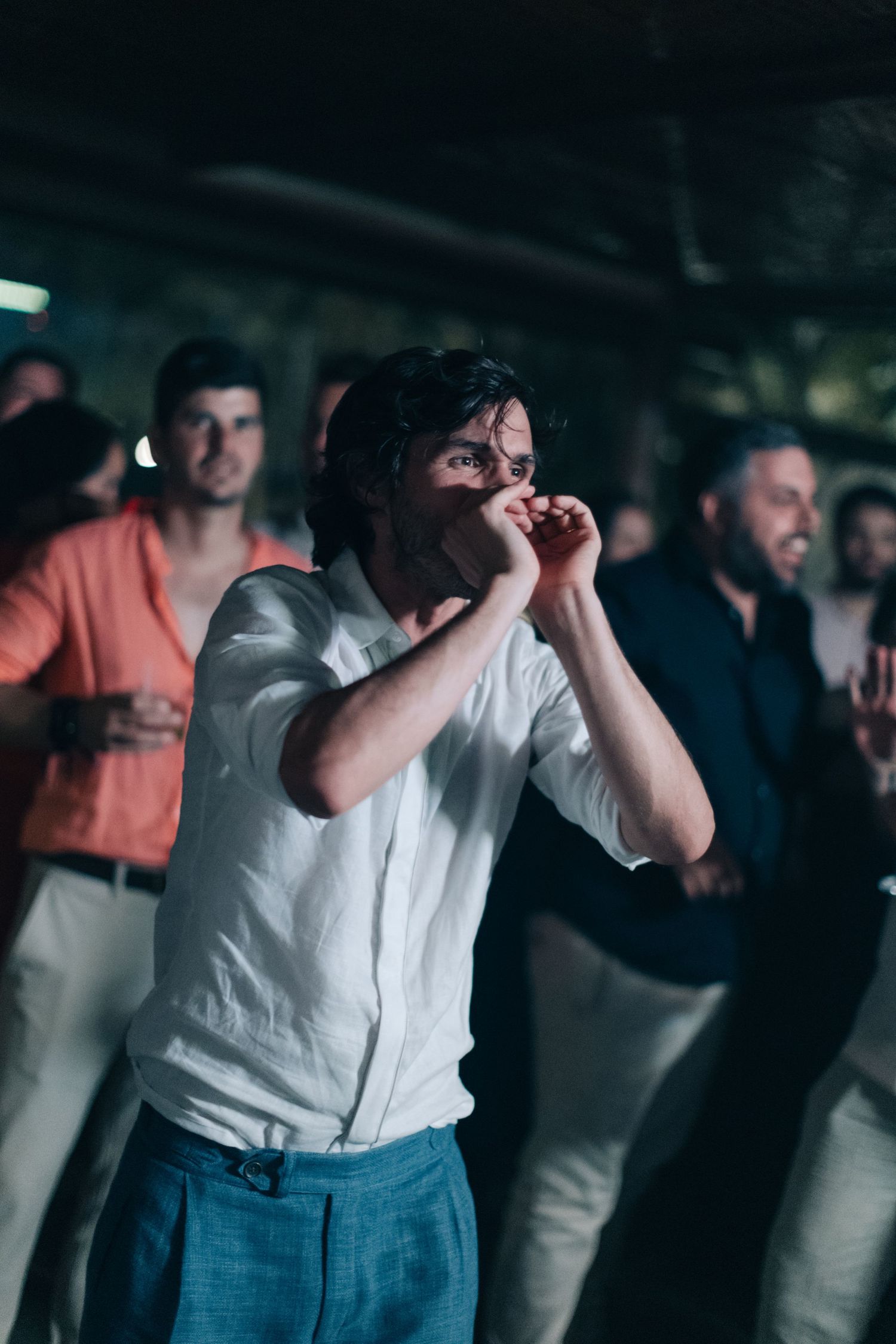 Wedding guests dancing energetically at a dimly lit reception venue.