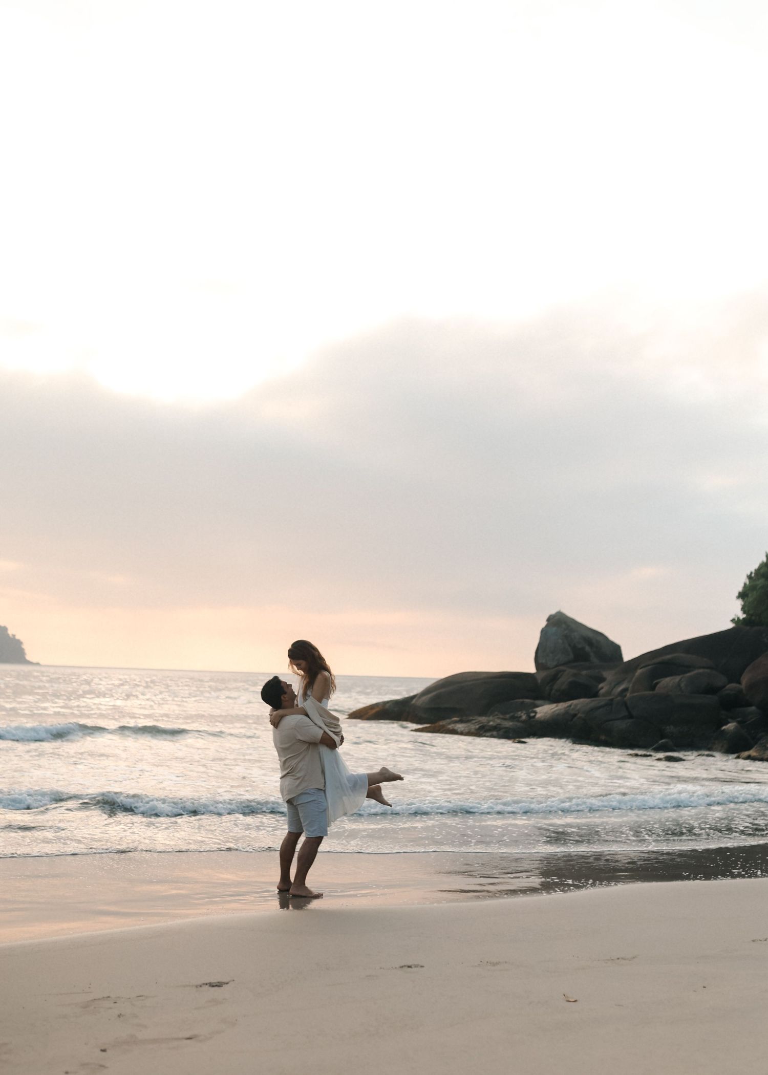 A romantic beach moment captured as a couple embraces near crashing waves at dusk.
