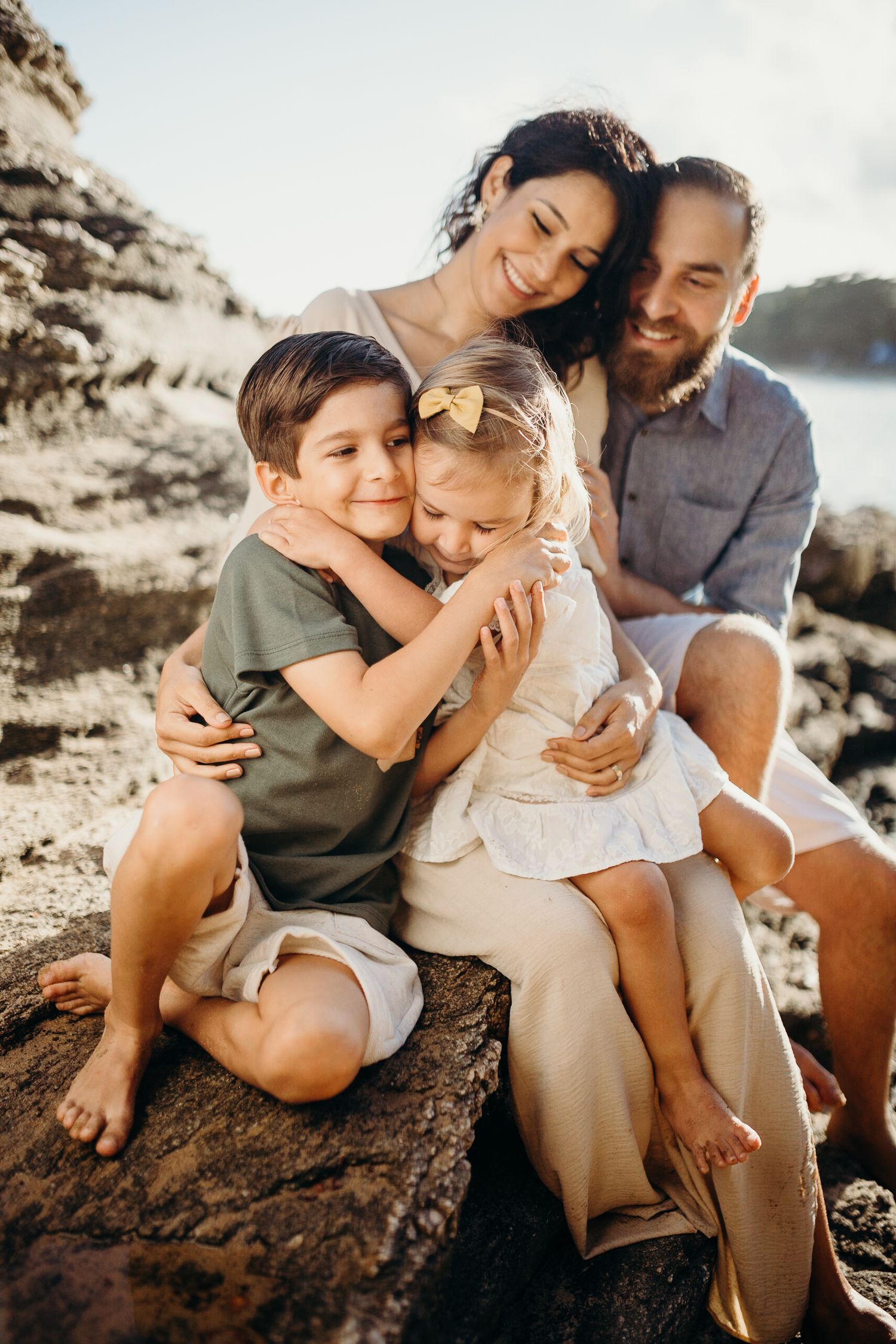Intimate family portraits showing loving embraces on a rocky beach setting.