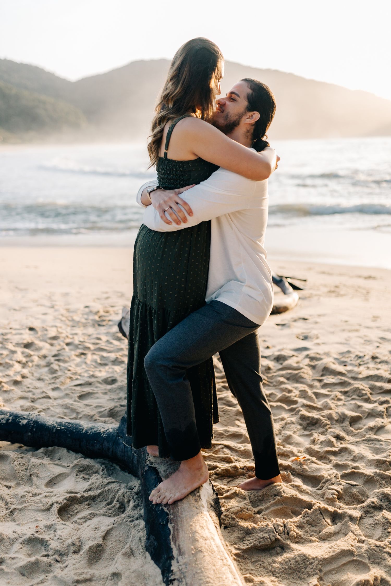 Romantic embrace on sandy beach during golden hour engagement photoshoot.