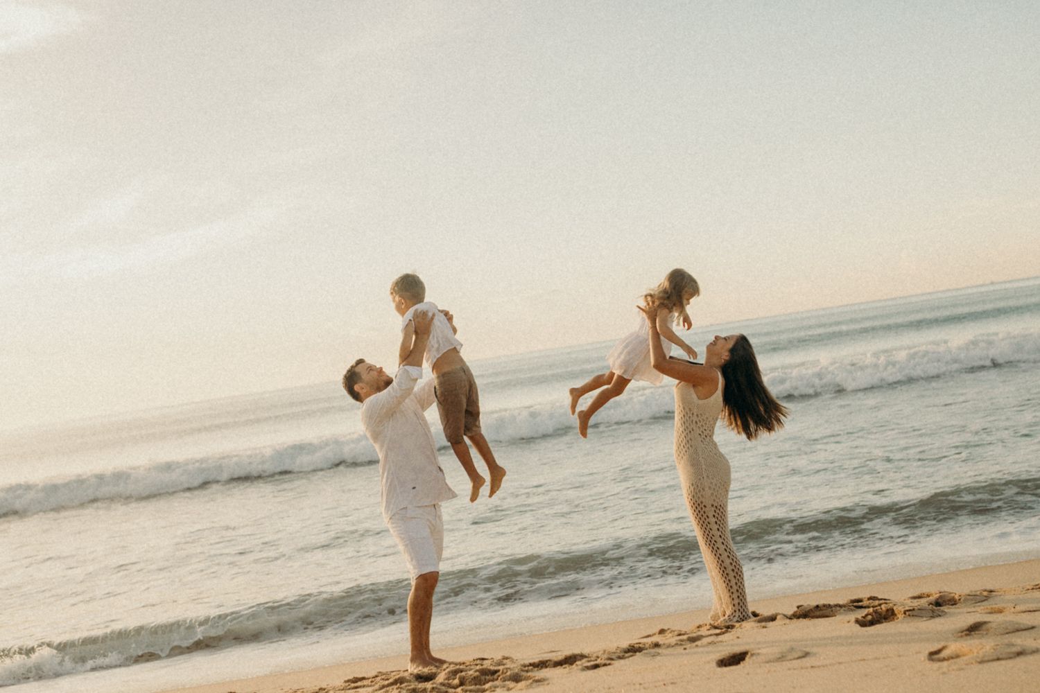 Parents lifting children while playing on beach during golden hour.
