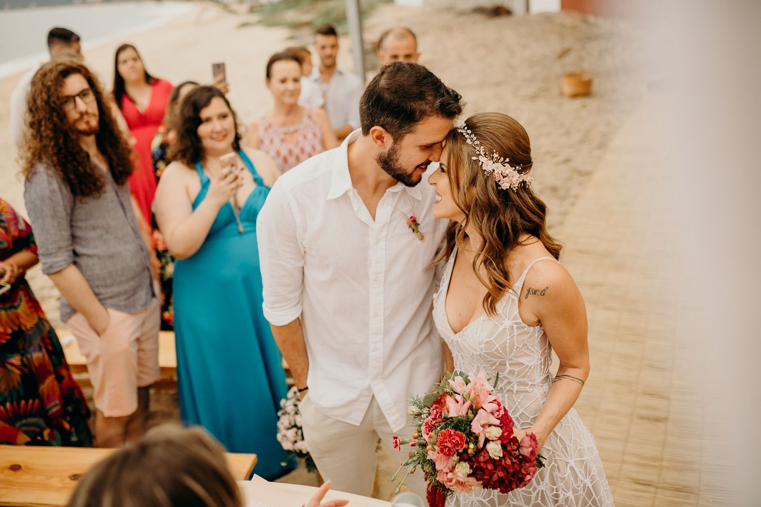 Intimate beachside wedding reception with guests seated at wooden tables.