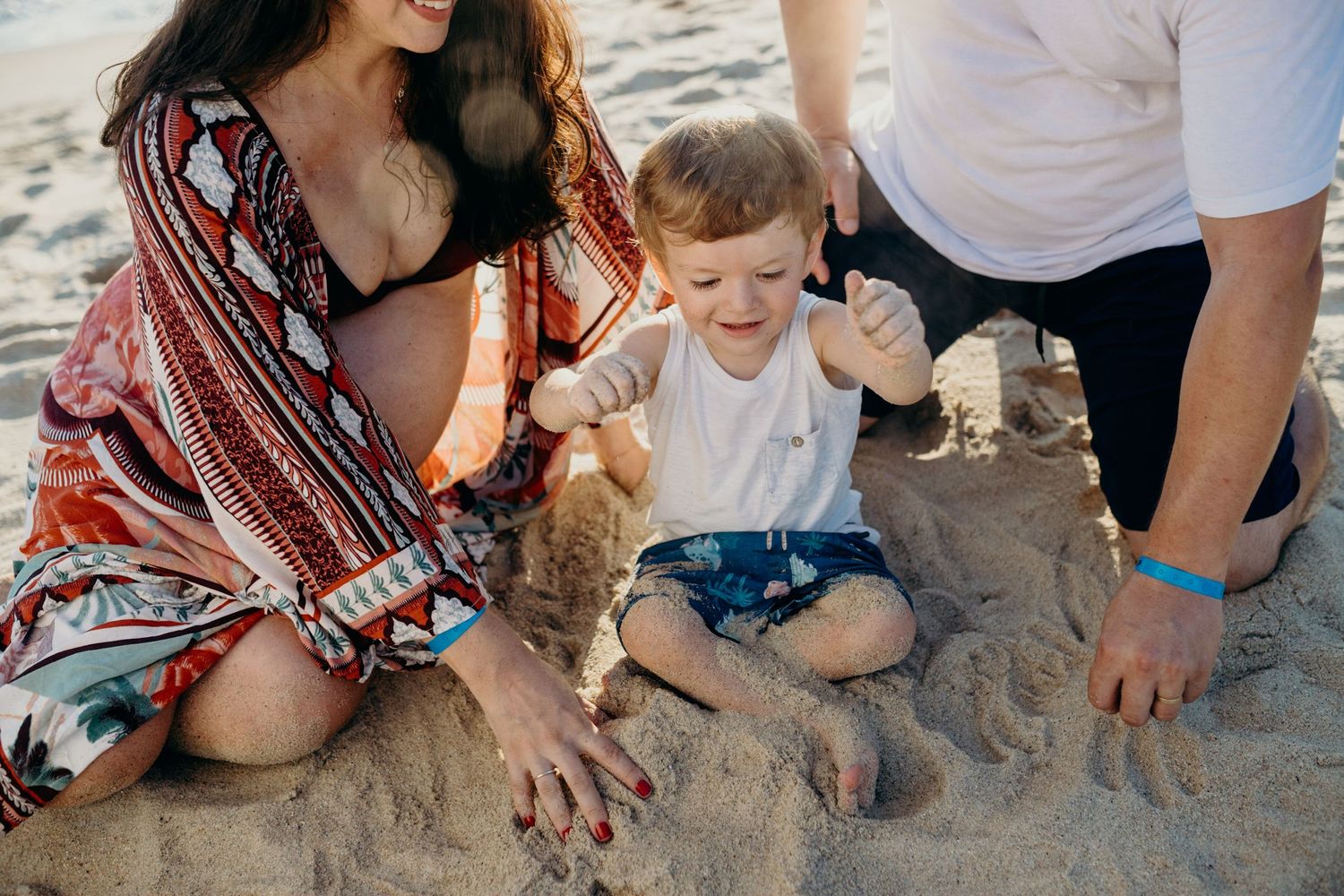 Family playing together in sand during golden hour at the beach.