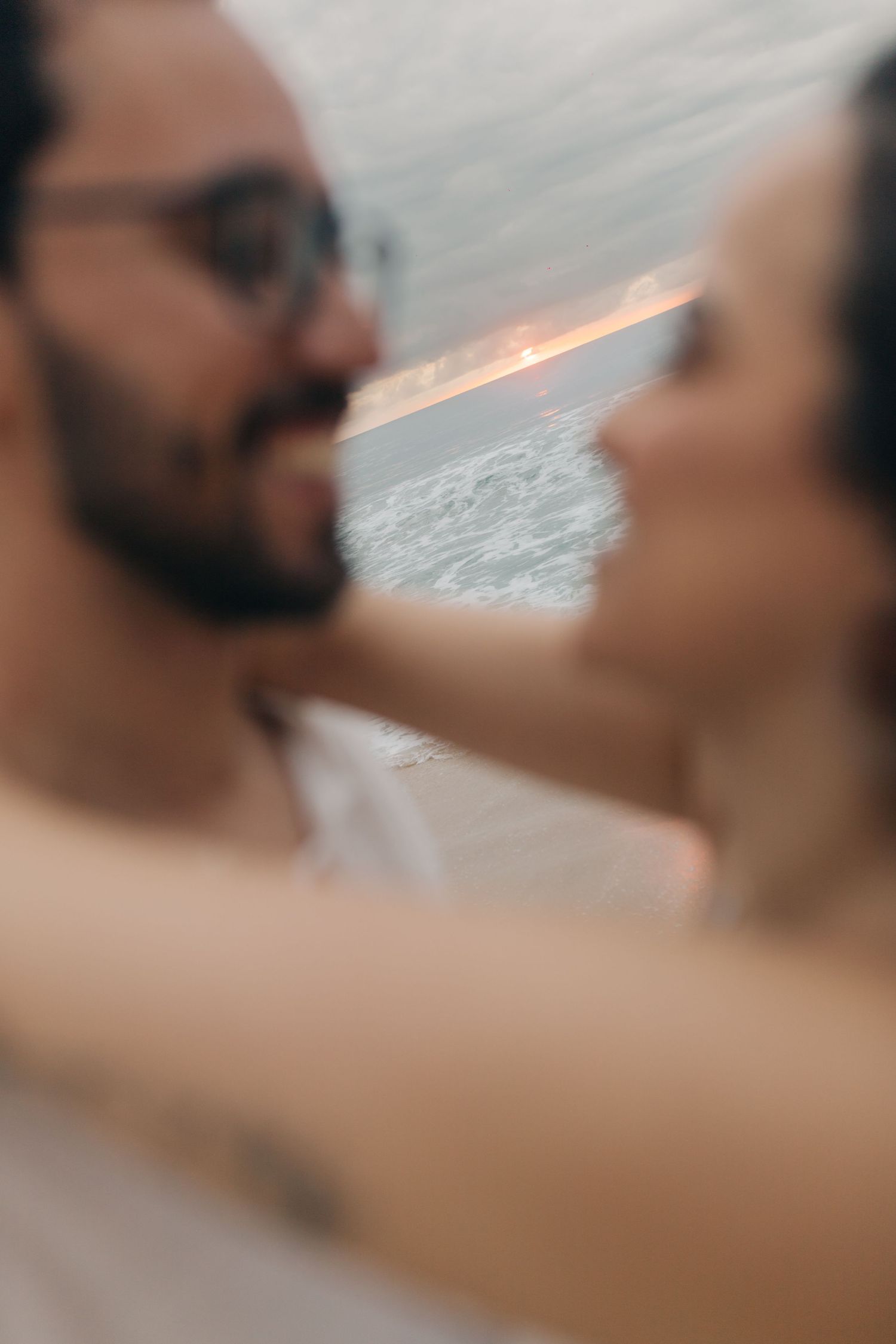 Close-up shot of a couple sharing an intimate moment on the beach at sunset.
