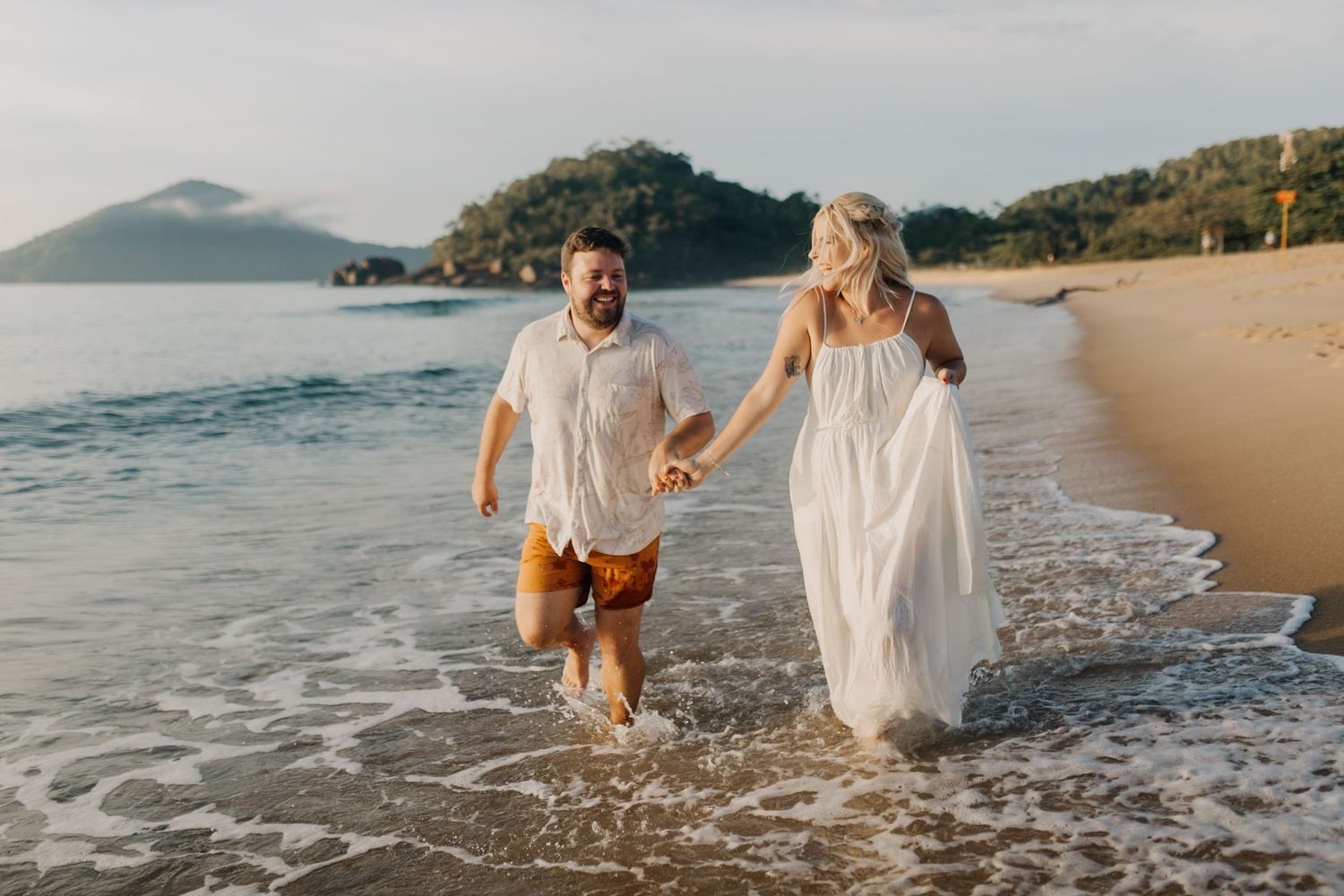 Intimate beach moment captured with couple walking through gentle waves along shoreline.