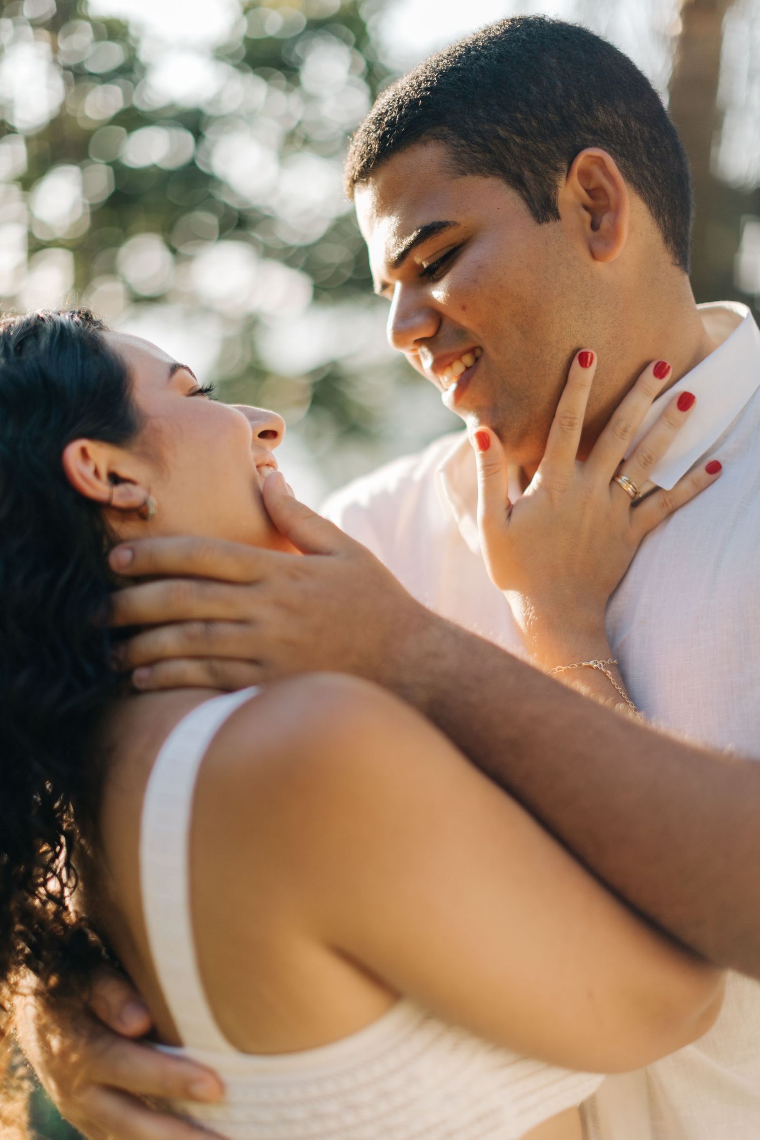 A romantic couple sharing an intimate moment outdoors with golden sunlight filtering through the trees.