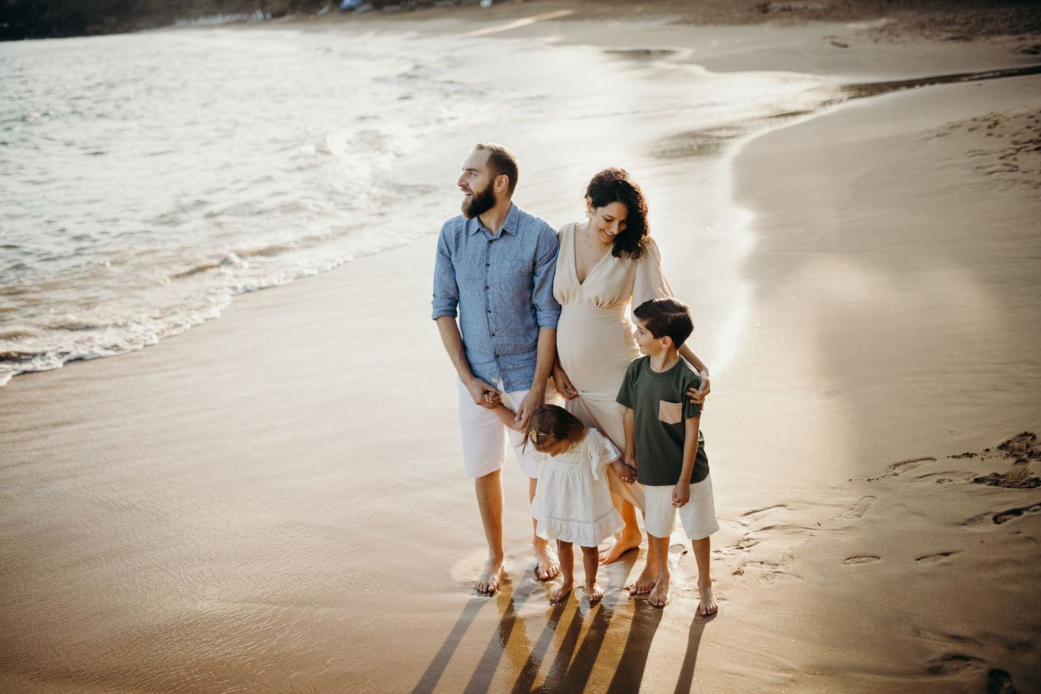 Family walking together on beach at sunset casting long shadows in the sand.