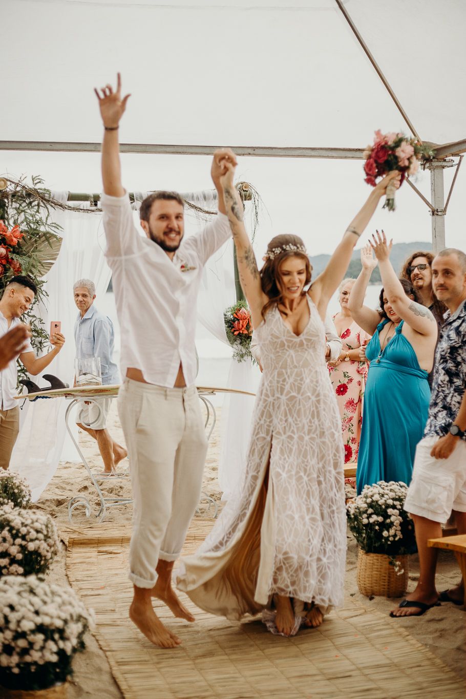Joyous celebration with wedding guests dancing and raising their hands under a seaside tent.