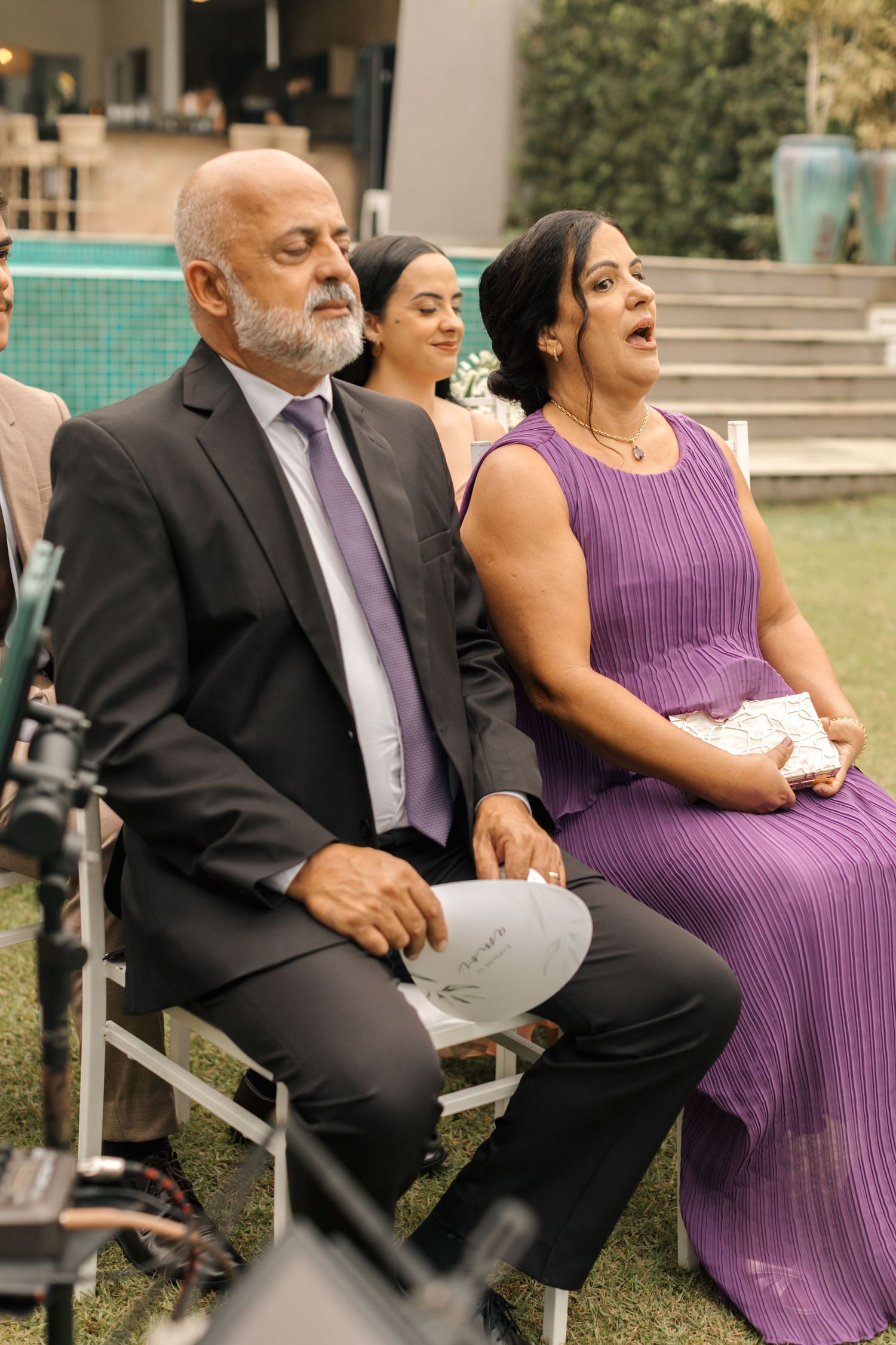 Wedding guests in purple attire sharing laughs during an outdoor ceremony.
