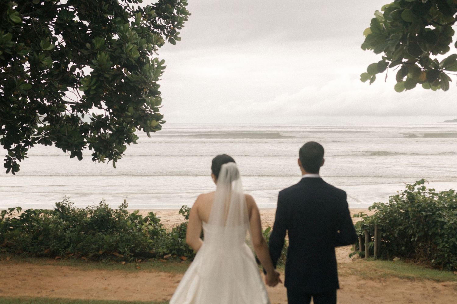 A couple holds hands while looking at the ocean view during their wedding photoshoot.