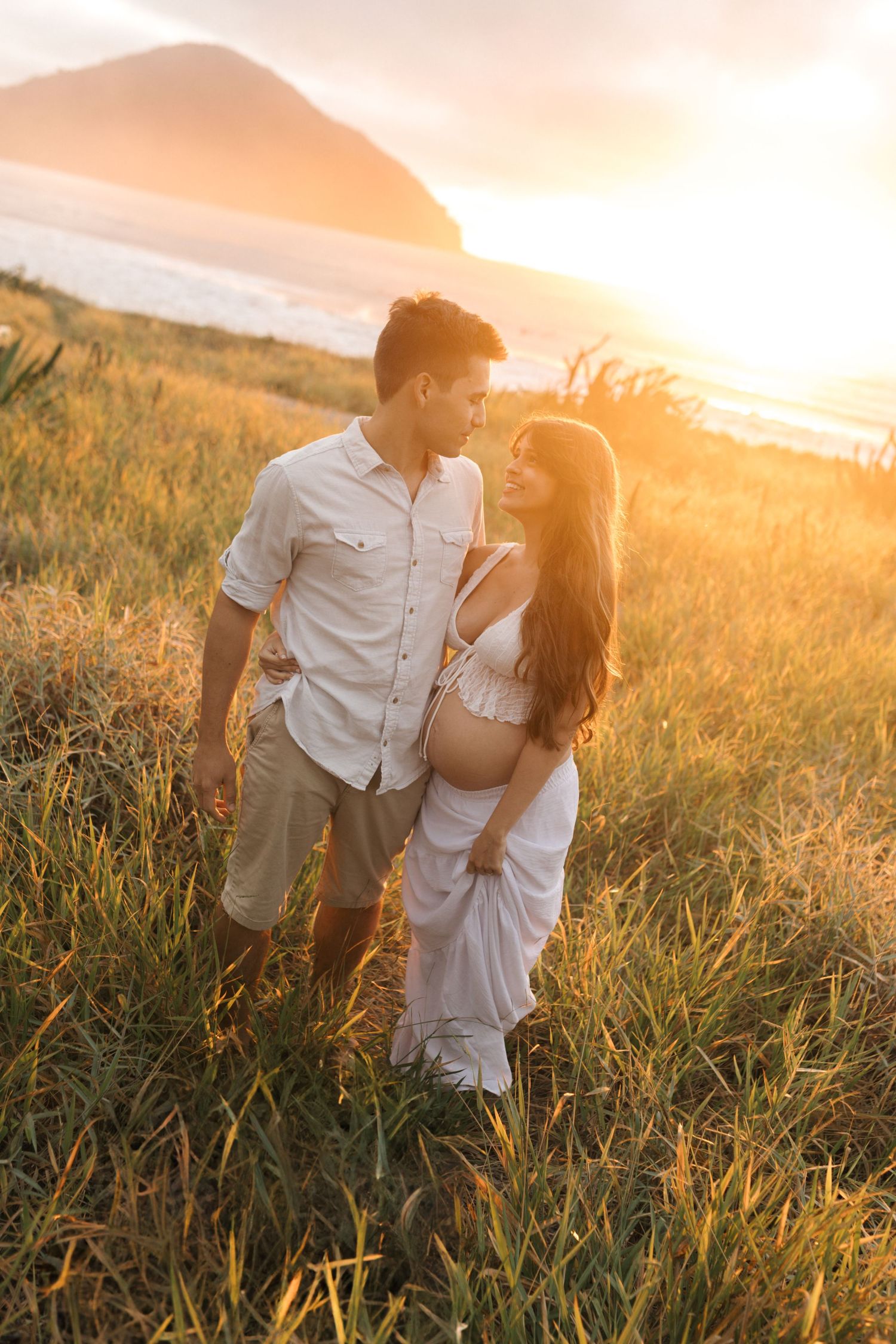 Romantic couple embracing in a golden field at sunset with warm sunlit glow behind them.