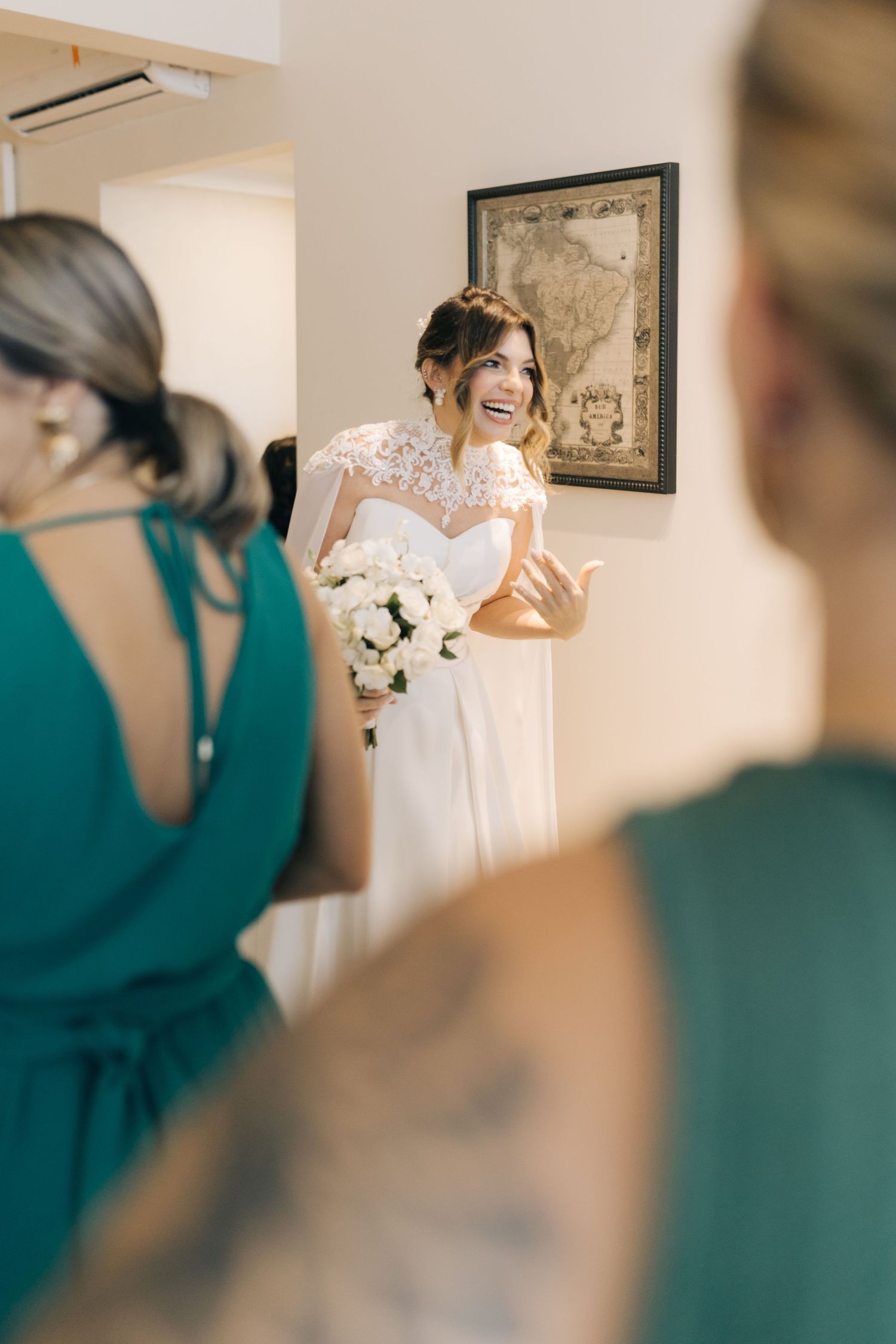 A bride in a lace wedding gown shares a joyful moment with bridesmaids wearing emerald green dresses.
