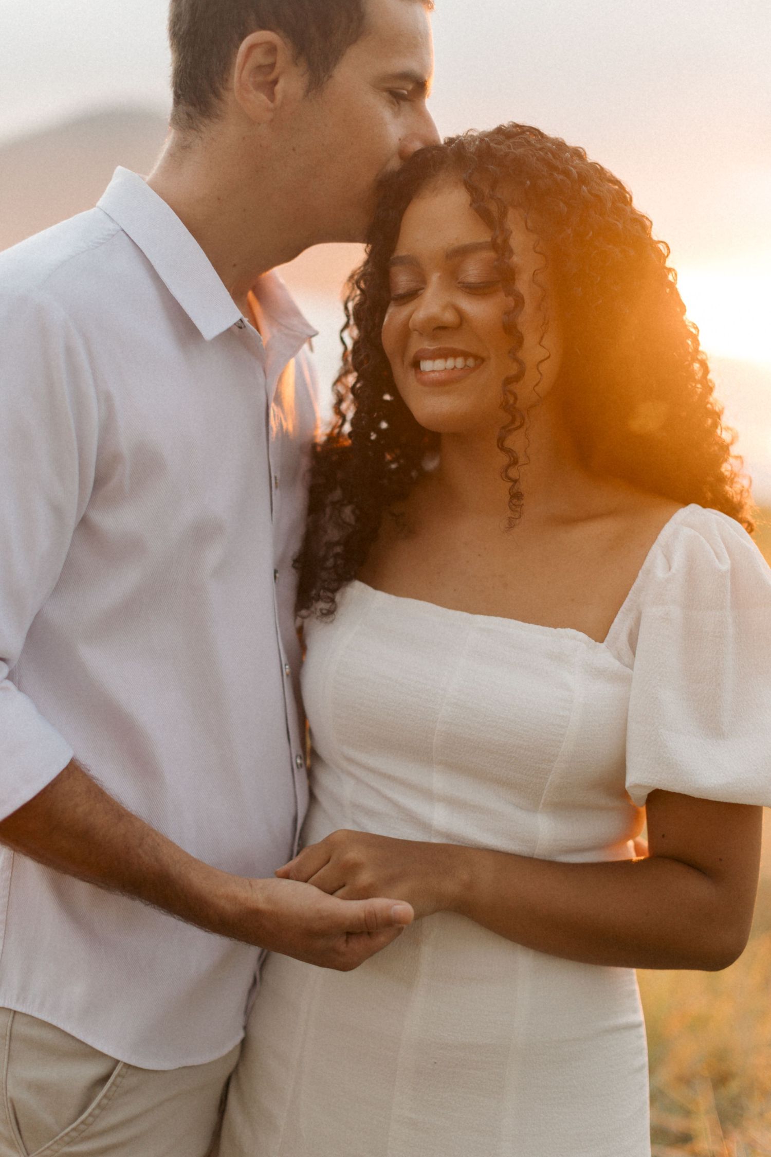 A romantic couple shares an intimate moment at sunset as warm golden light illuminates them against a dreamy background.