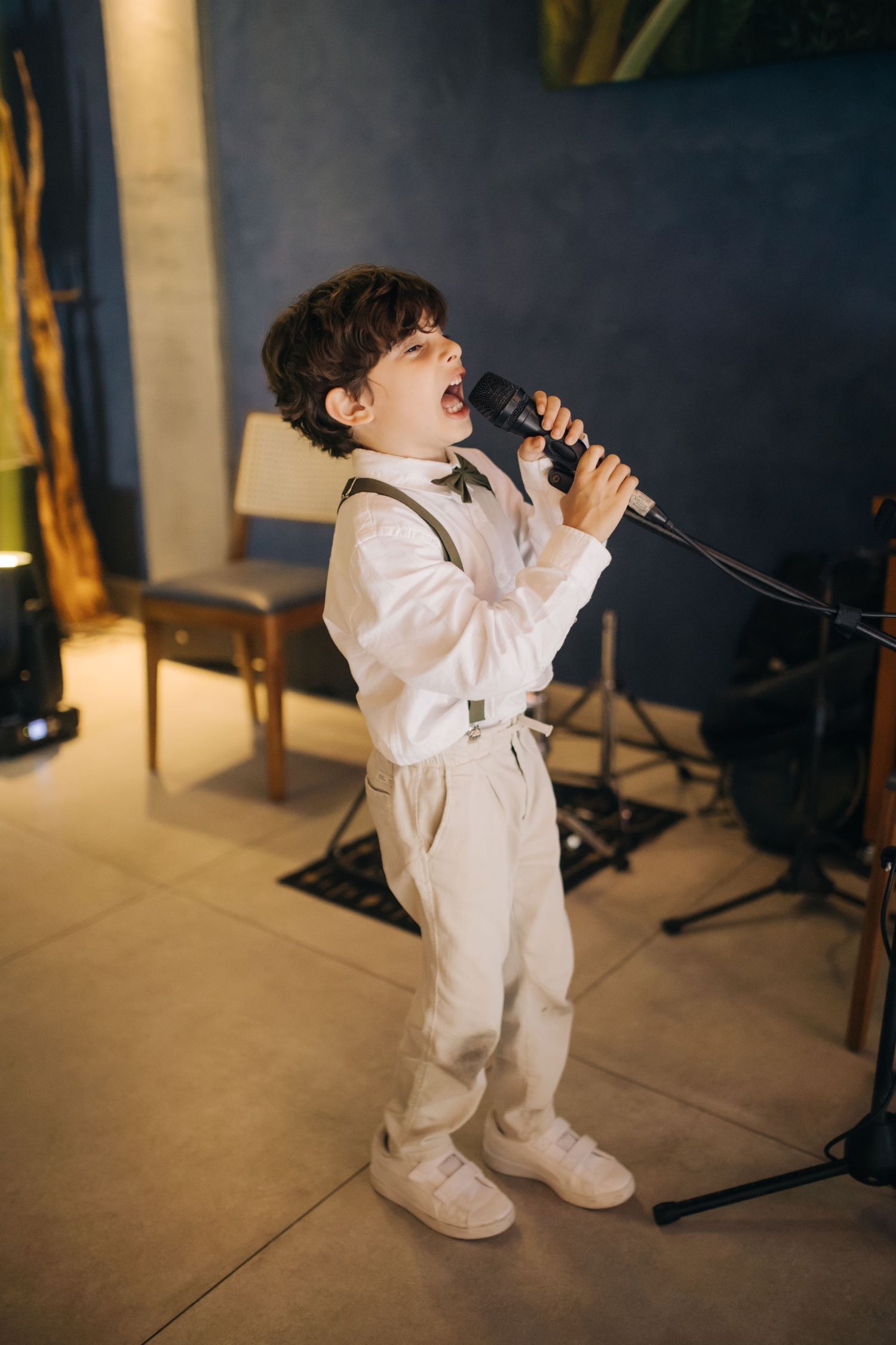 Young performer in white outfit singing passionately into microphone during wedding reception.