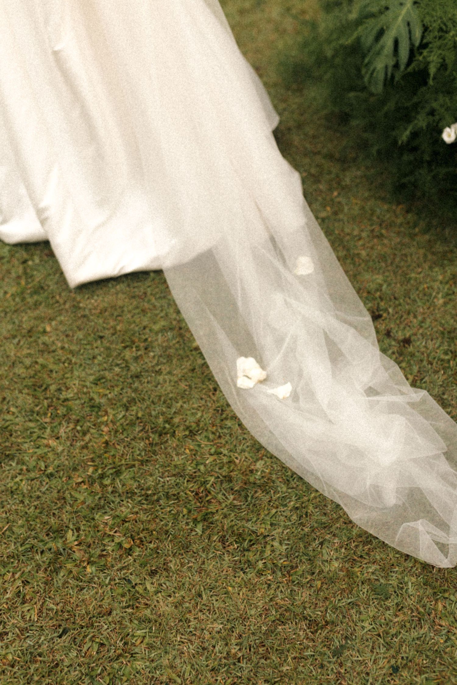 Close-up of white wedding dress train flowing across green grass.