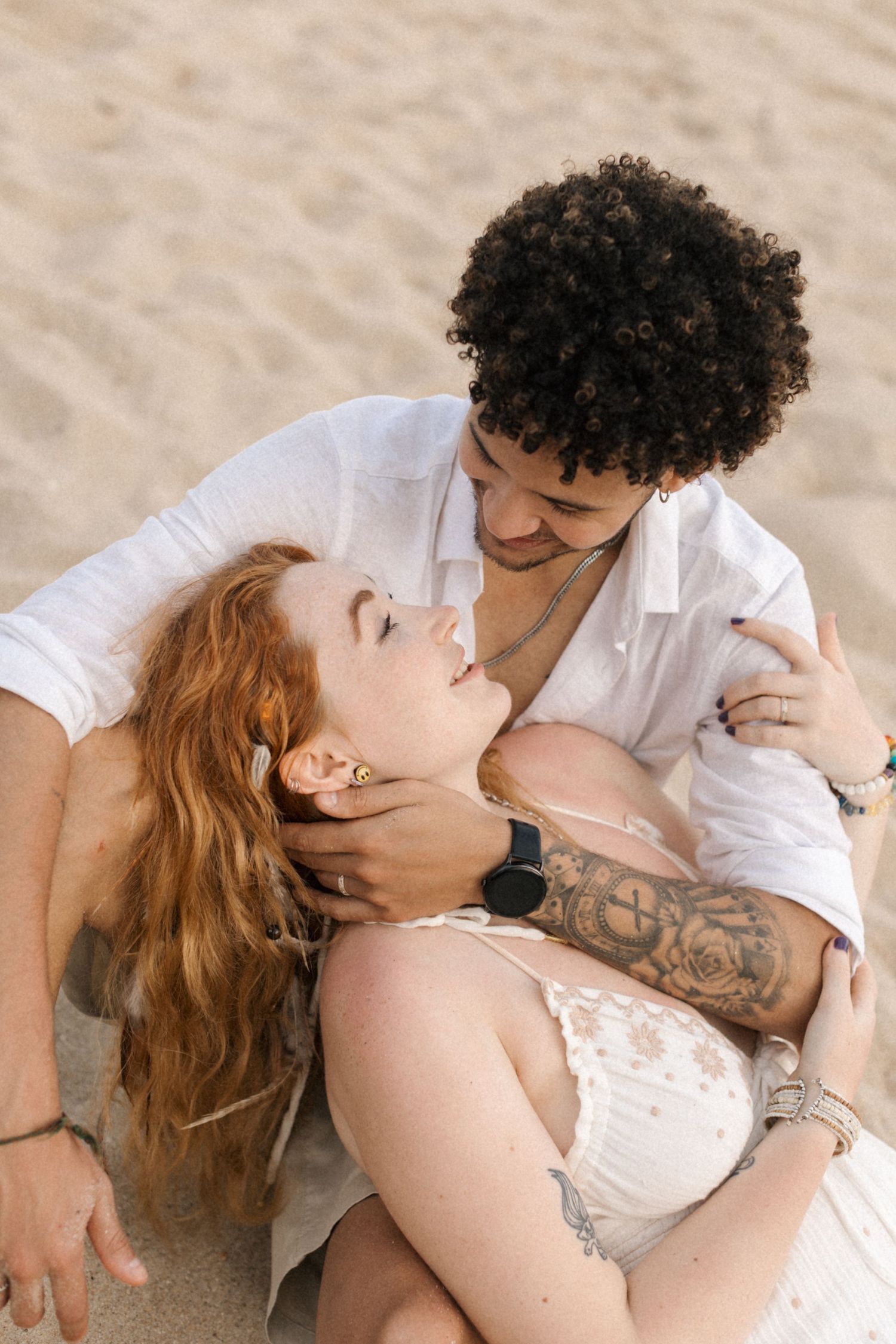 A couple shares an intimate moment while sitting on the beach sand.