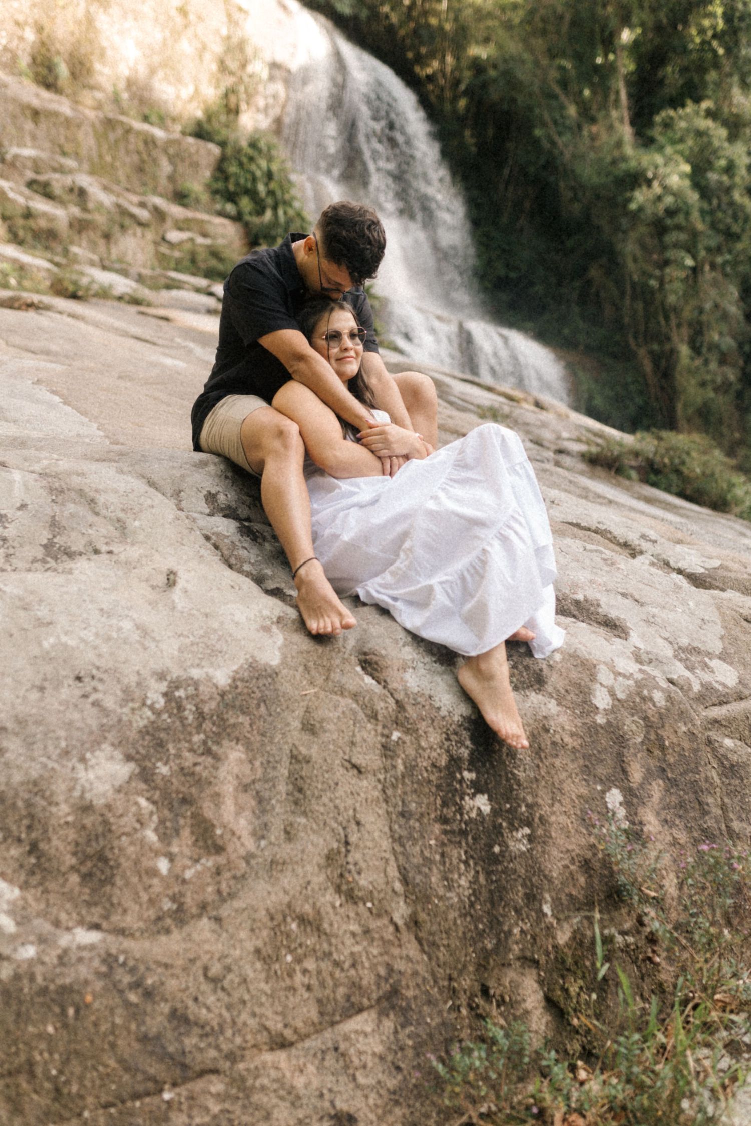 Candid moments of a couple reclining on rocks near a scenic waterfall.