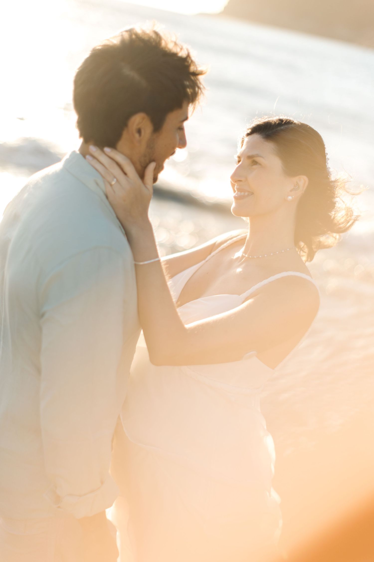 A couple embraces in golden sunlight during a romantic beach photoshoot at sunset.