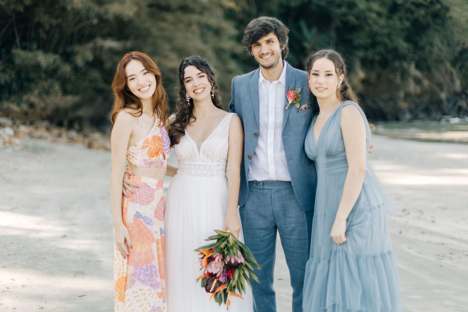 Wedding party members in coordinated blue and floral attire pose on sandy beach.