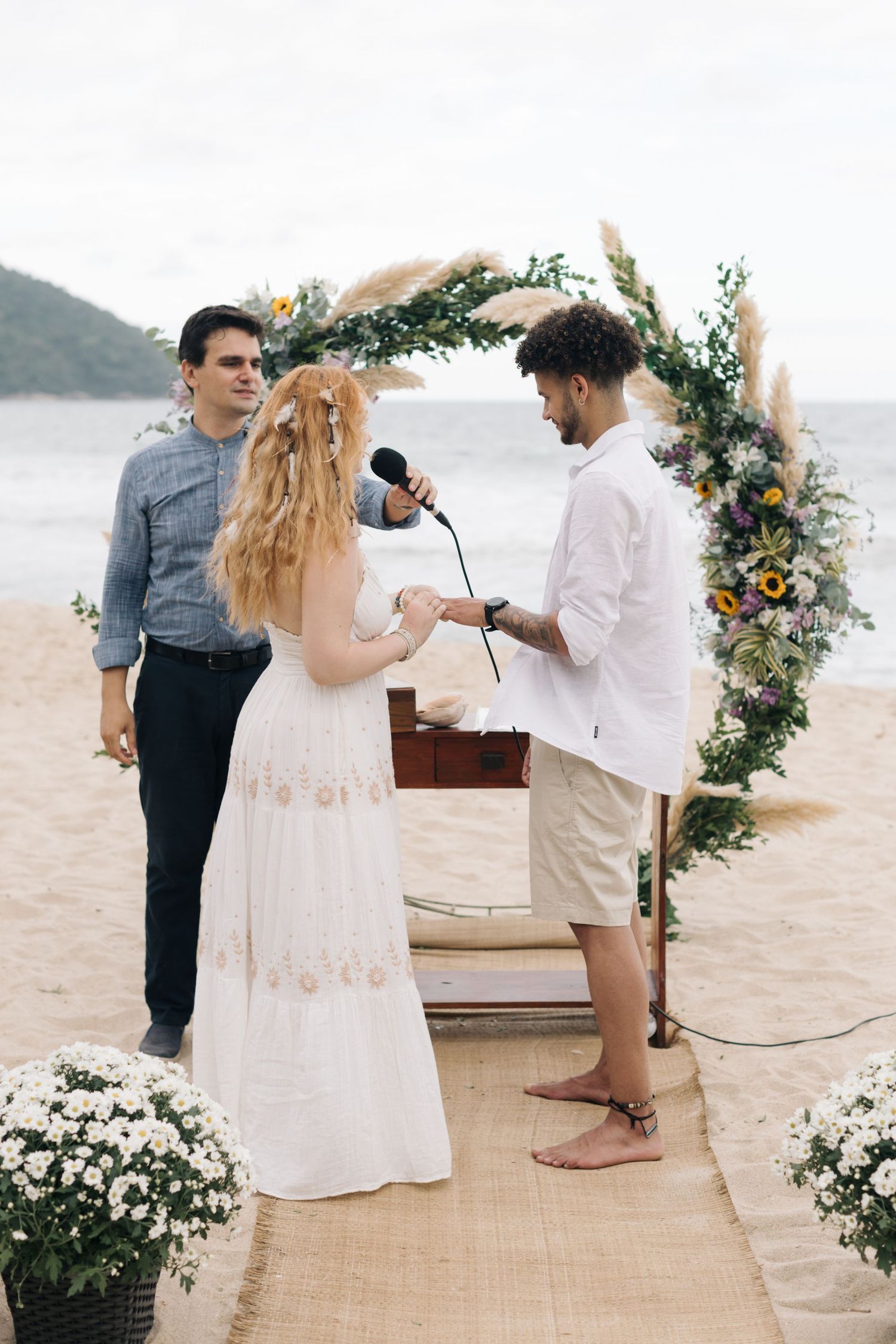 Beach wedding ceremony with floral arch, burlap aisle runner, and mountains in the background.