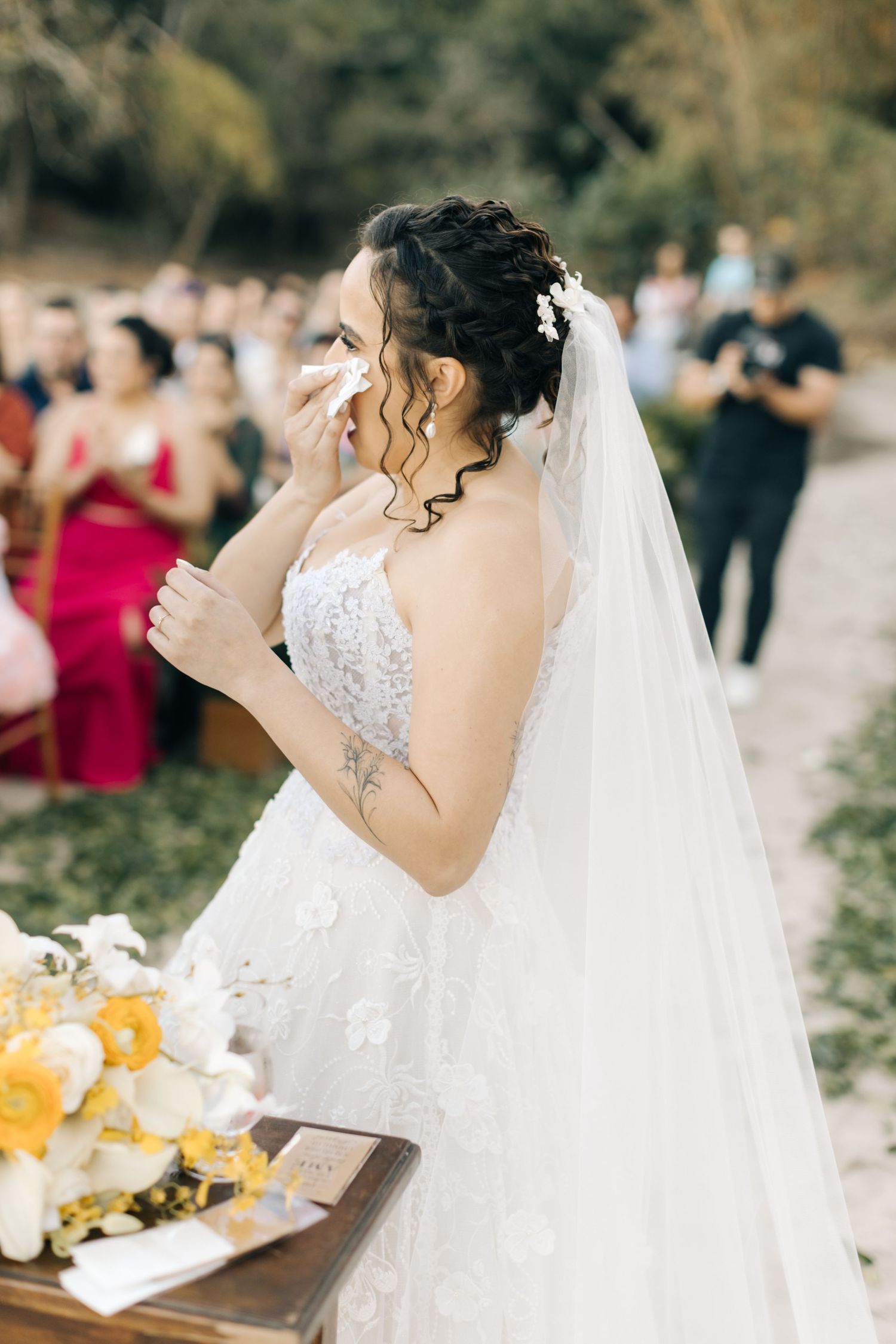 Bride in flowing white dress reads vows during outdoor beach ceremony.