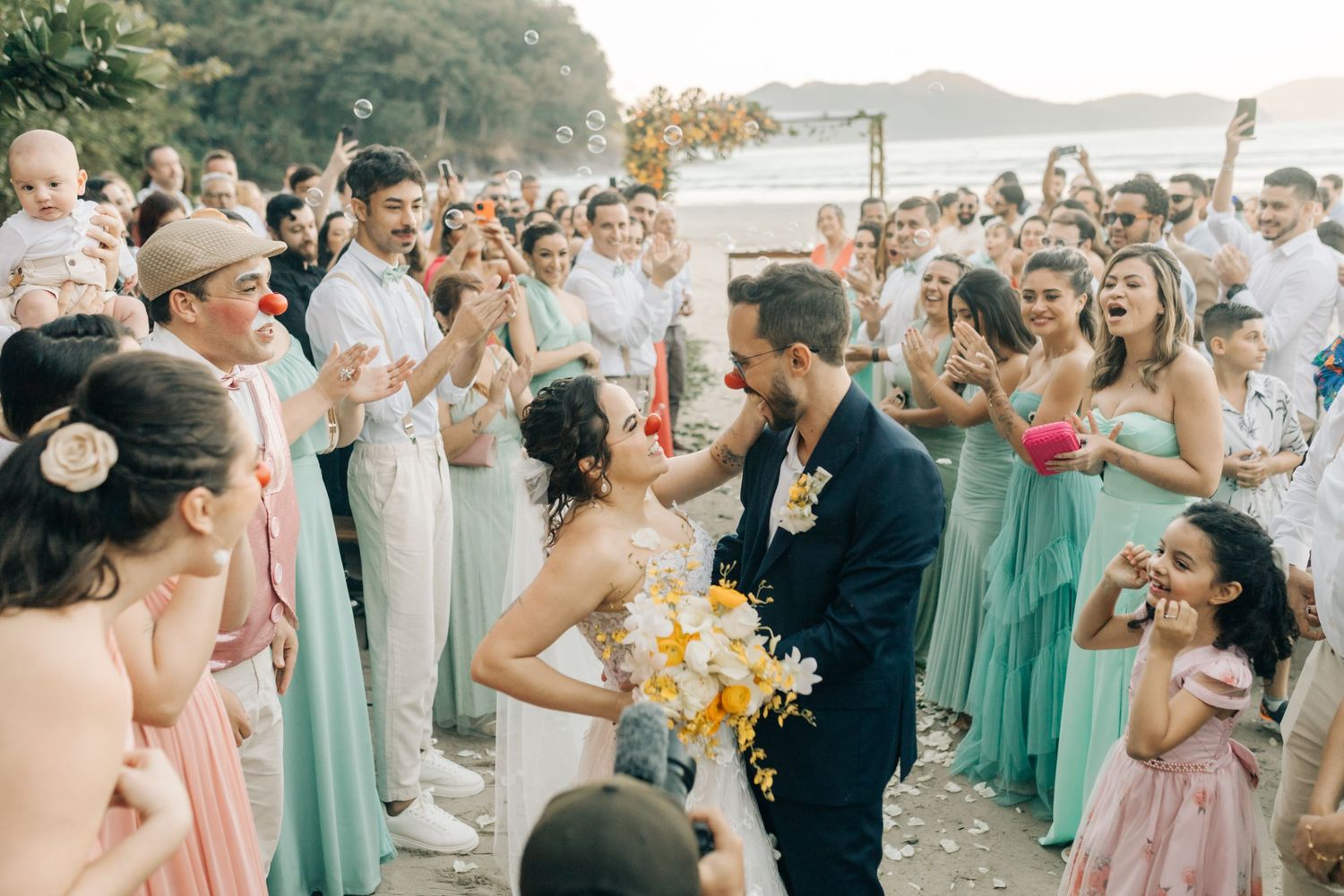 A romantic beachside wedding moment surrounded by guests in pastel bridesmaid dresses.