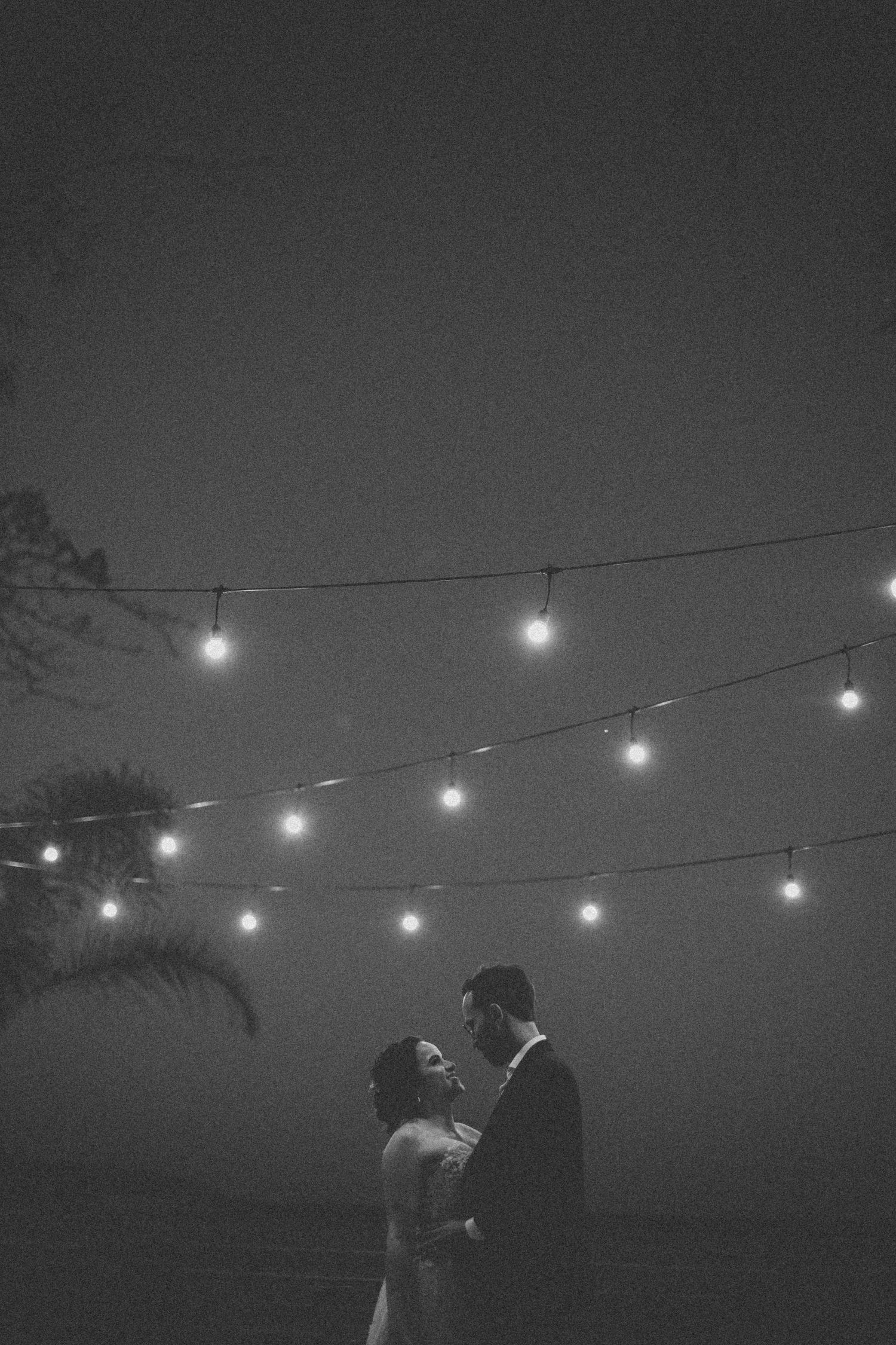 String lights illuminate a romantic outdoor scene under a dark evening sky.