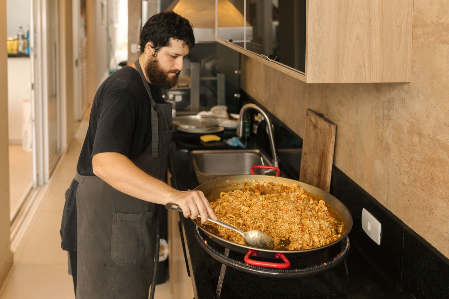 Chef preparing a large paella dish in a commercial kitchen setting.