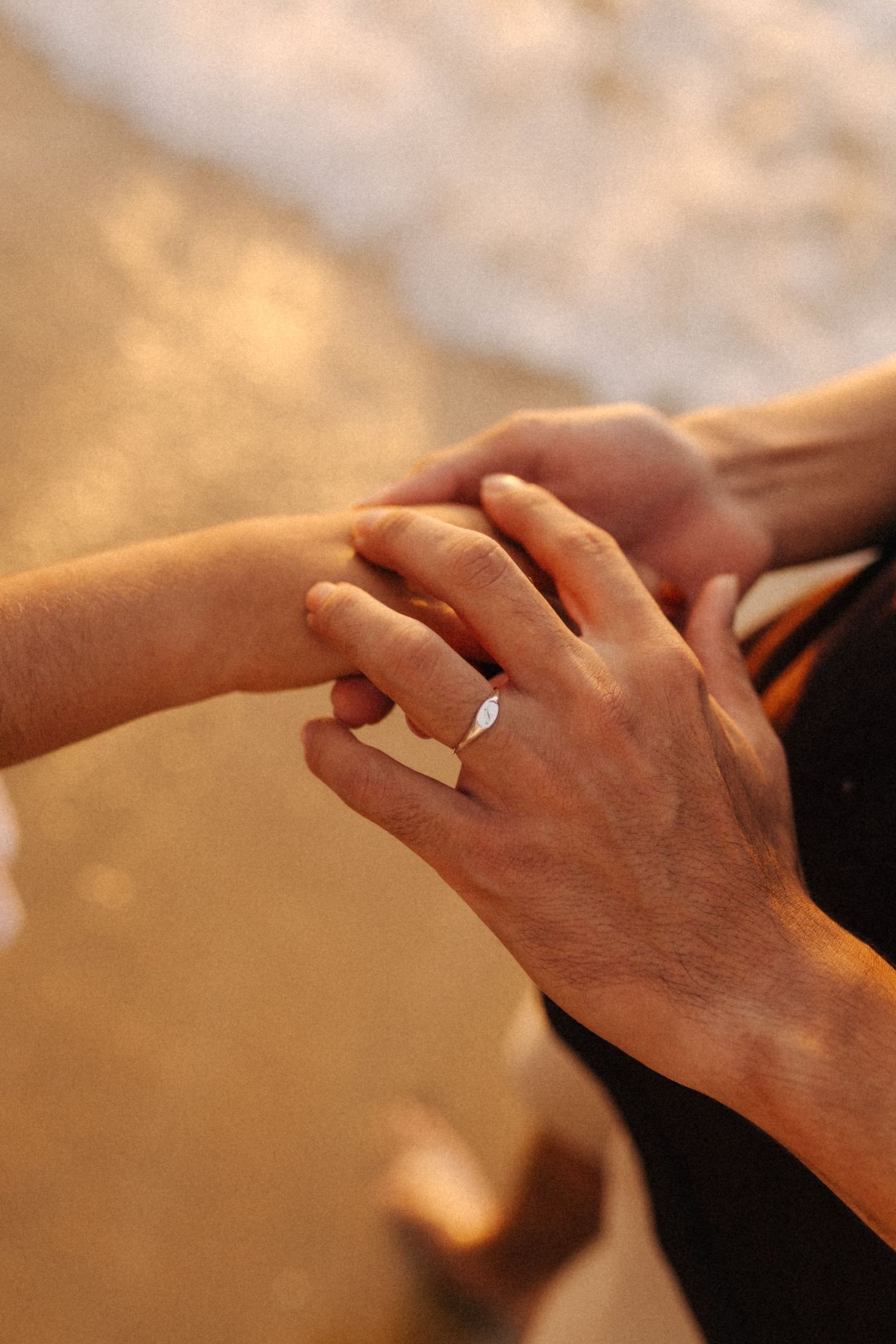 Duas mãos entrelaçadas com uma aliança de casamento visível em um momento íntimo de tons quentes.