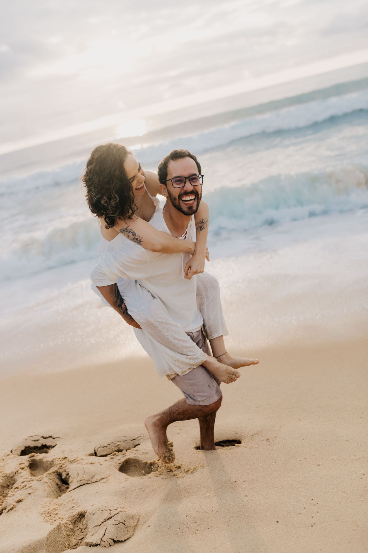 A playful piggyback ride on the beach with waves crashing in the background.